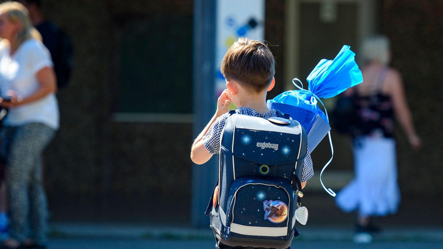 Ein Kind steht mit blauer Schultüte und Schultüte auf dem Schulhof