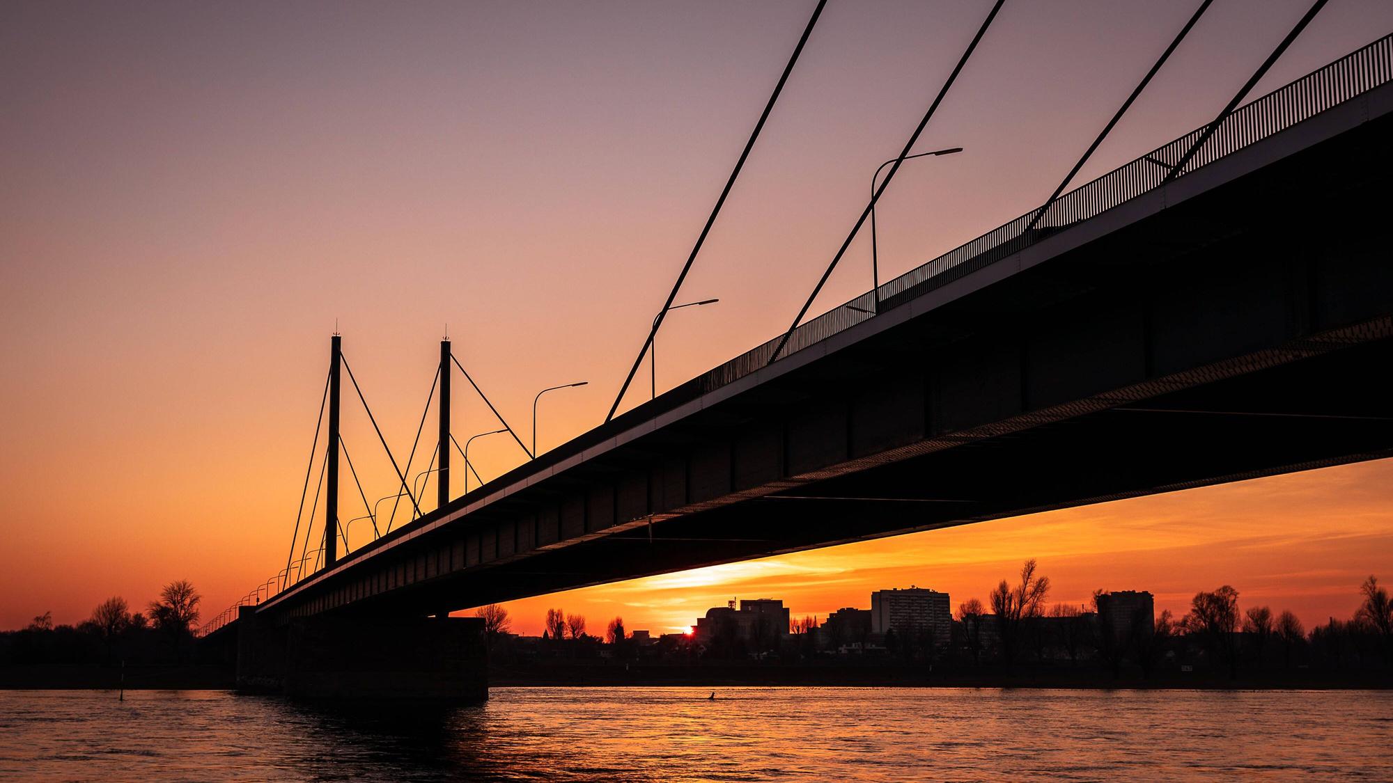 Hinter der Theodor-Heuss-Brücke in Düsseldorf geht die Sonne unter.