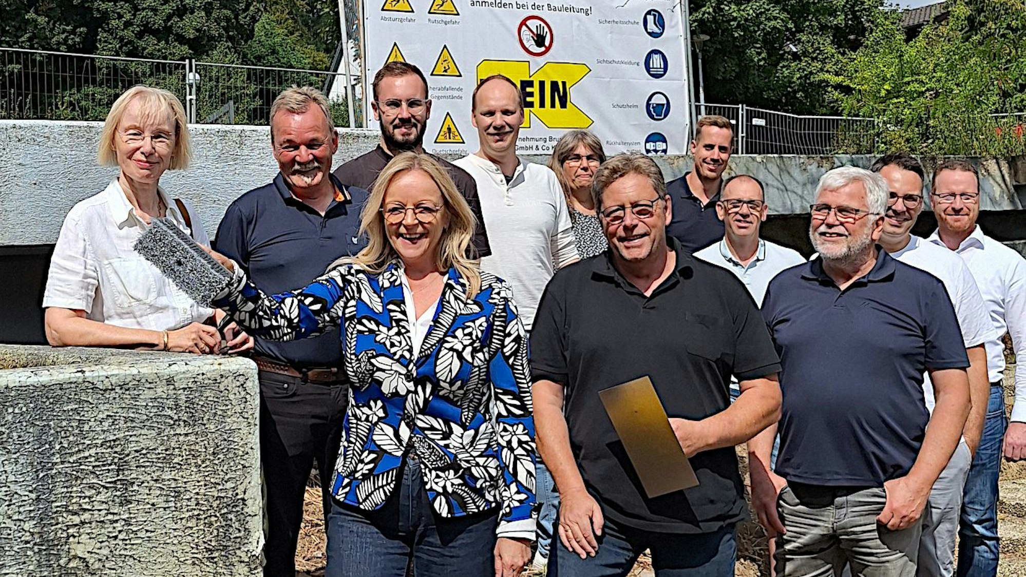 Eine Gruppe Menschen steht auf der Baustelle, Sabiner Preiser-Marian hat einen Malerquast in der Hand.