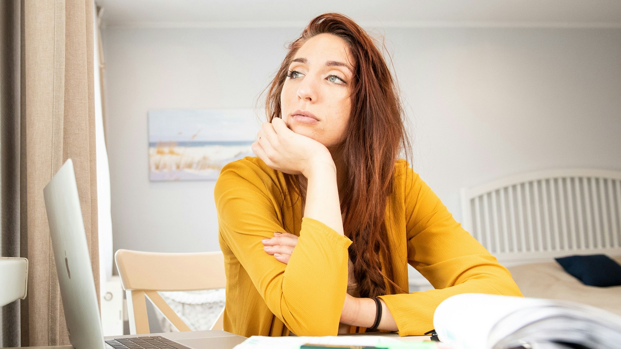 Eine Frau sitzt an einem vollen Schreibtisch und starrt in die Leere.