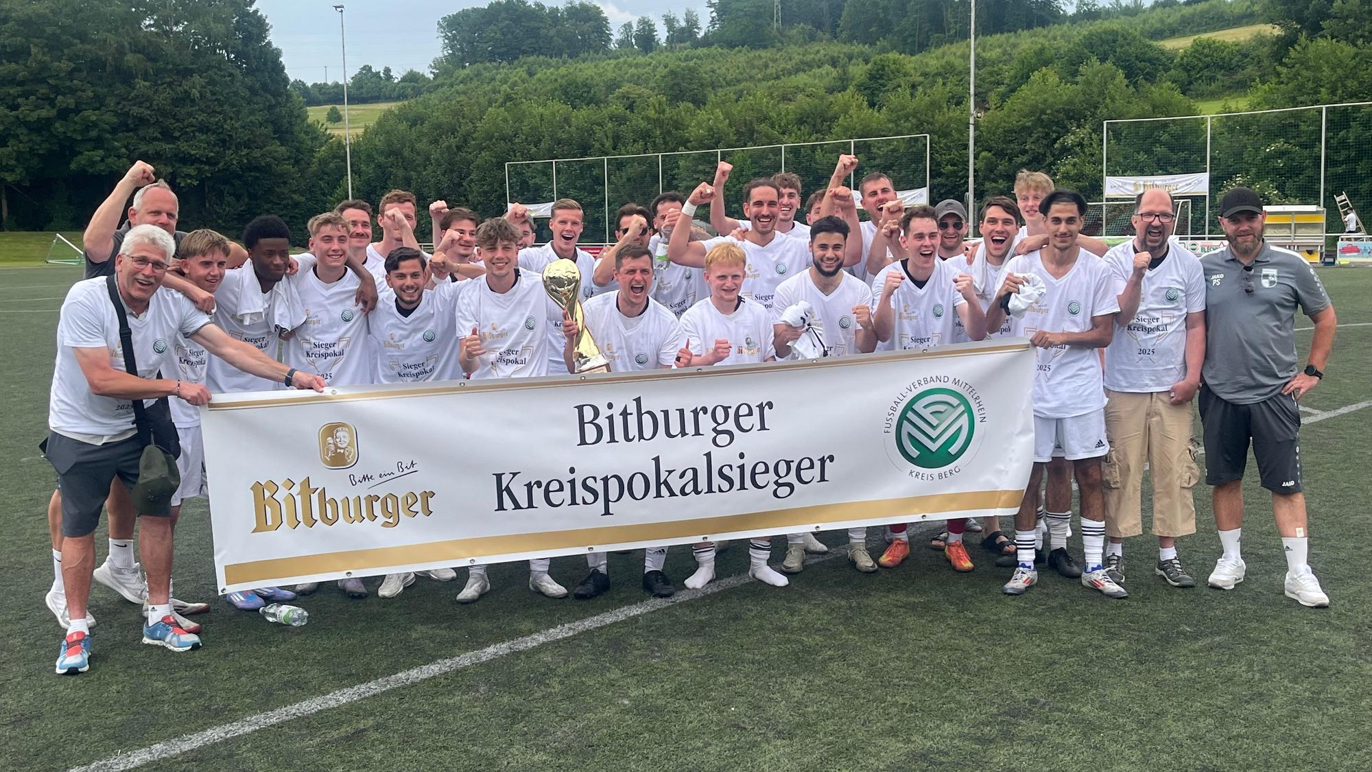 Die Fußballer des FV Wiehl feiern hinter einem Transparent den Kreismeistertitel.