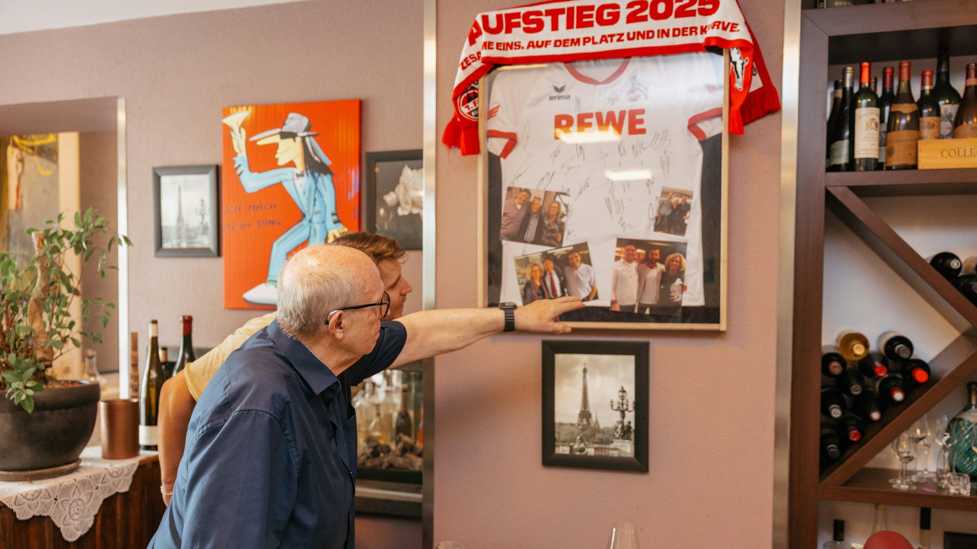 Dem Rivalen nah: Reiner Calmund (links) wirft einen Blick auf das Köln-Trikot an der Wand. „Calli“ stellte dem befreundeten Restaurantbesitzer Uwe Kern etwa Torwartlegende Toni Schumacher vor, im Bilderrahmen unten links zu sehen.