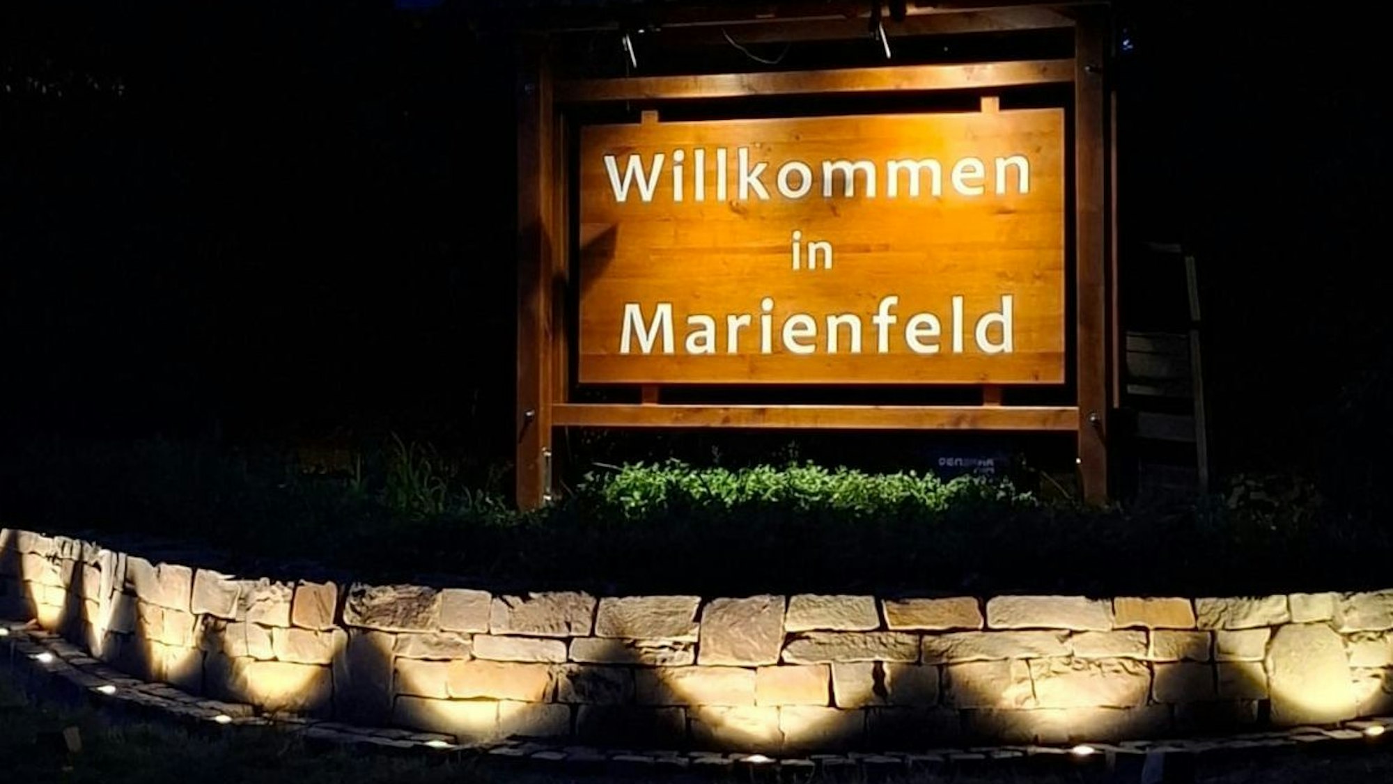 Abends wird das Willkommens-Schild und die Naturstein-Mauer beleuchtet.