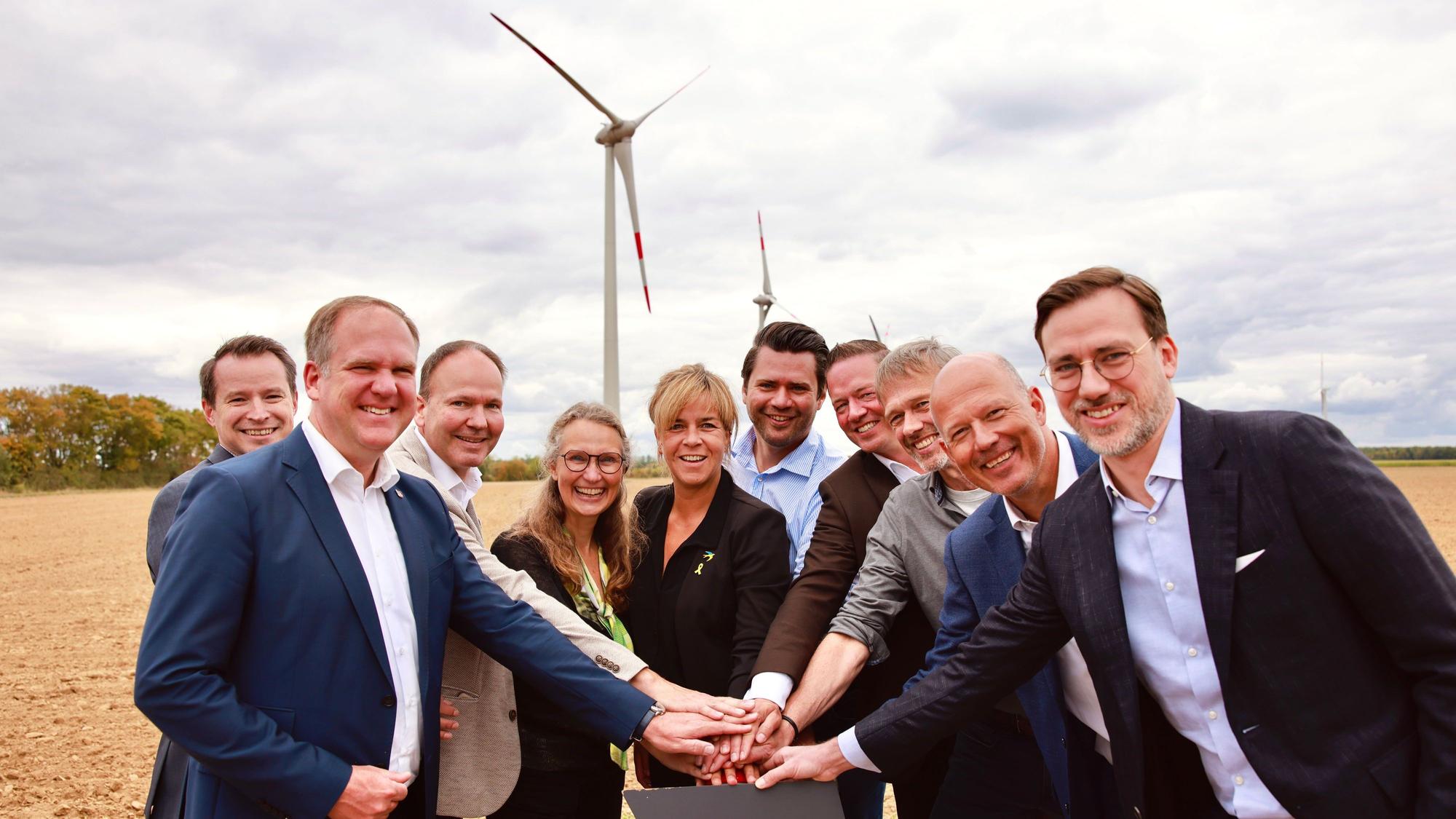 Das Foto zeigt die Vertreter der Unternehmen und aus der Politik beim symbolischen Knopfdruck, im Hintergrund die Windräder.