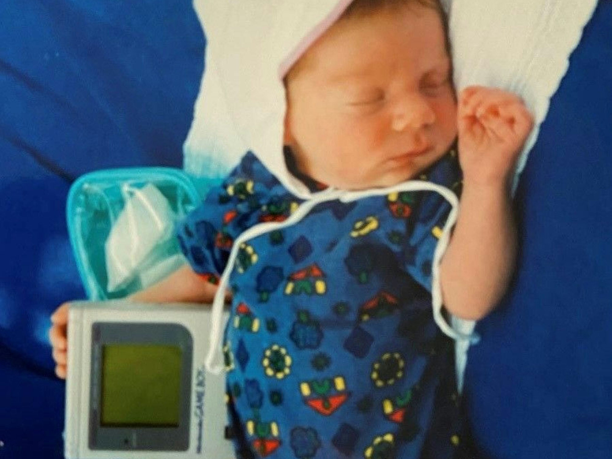Ein schlafende Baby hält einen Gameboy im Arm.