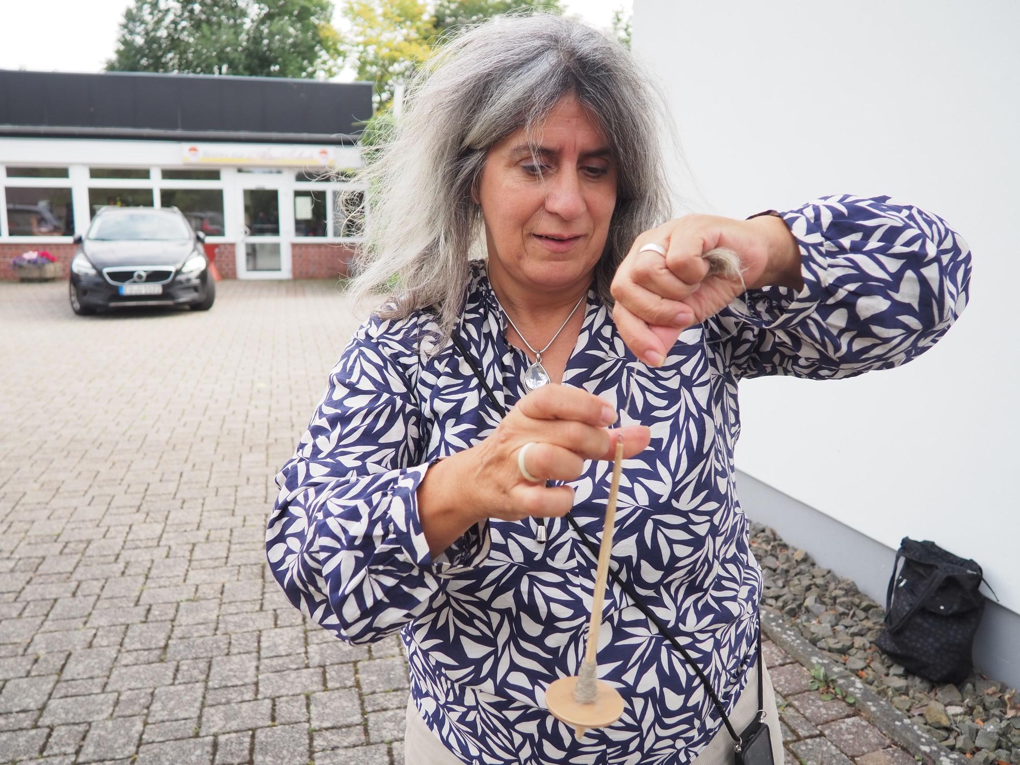 Teresa Funhas hat eine Spindel in der Hand und spinnt einen Faden aus Flachsfasern.
