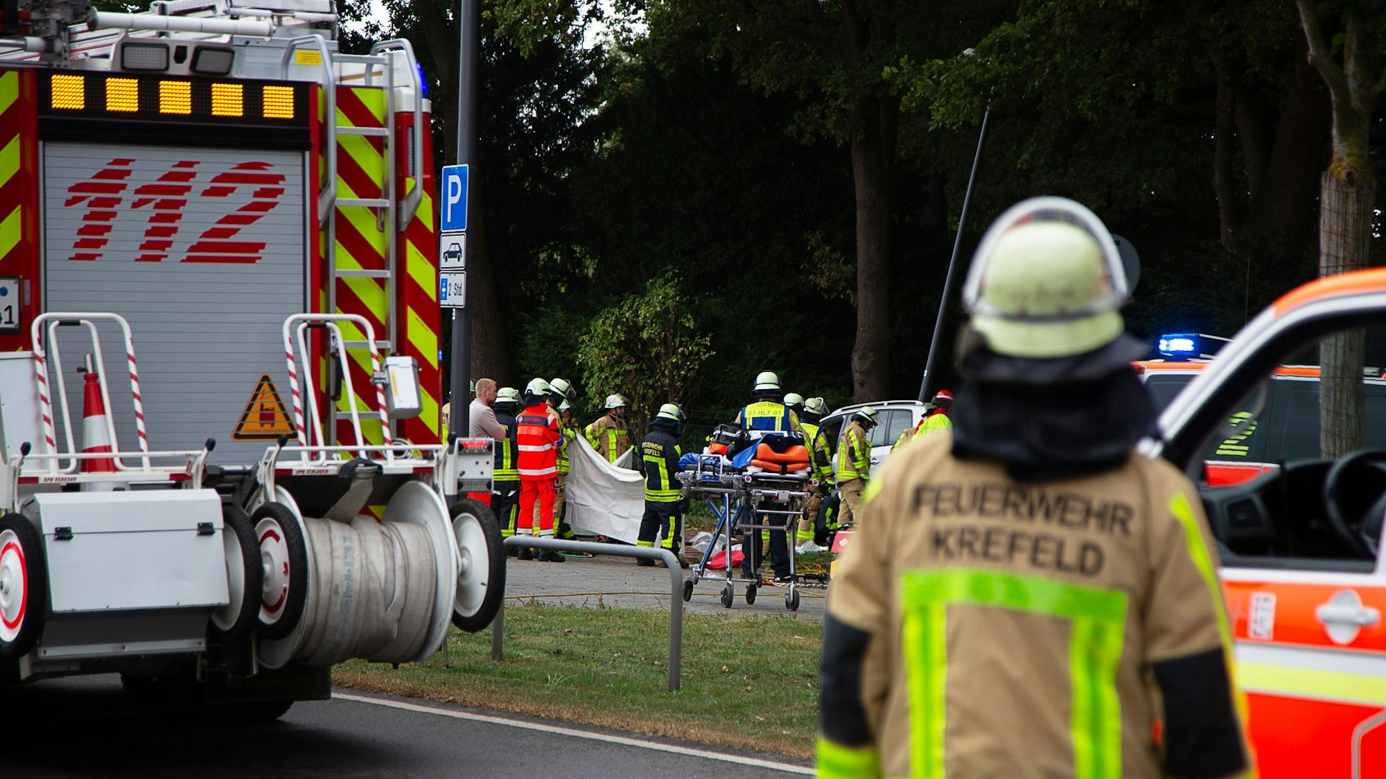 Kräfte der Feuerwehr sind am Friedhof Gellep-Stratum an der Unfallstelle im Einsatz. Auf dem Parkplatz des Friedhofs ist ein Auto in eine Menschenmenge gefahren.