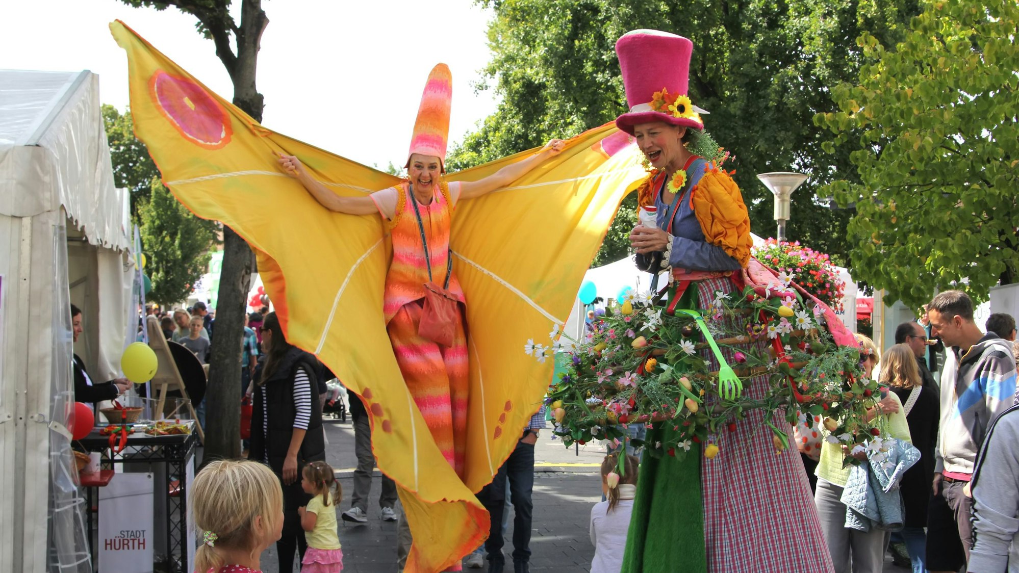 Das Foto zeigt zwei bunt kostümierte Frauen auf Stelzen vor dem Medio.
