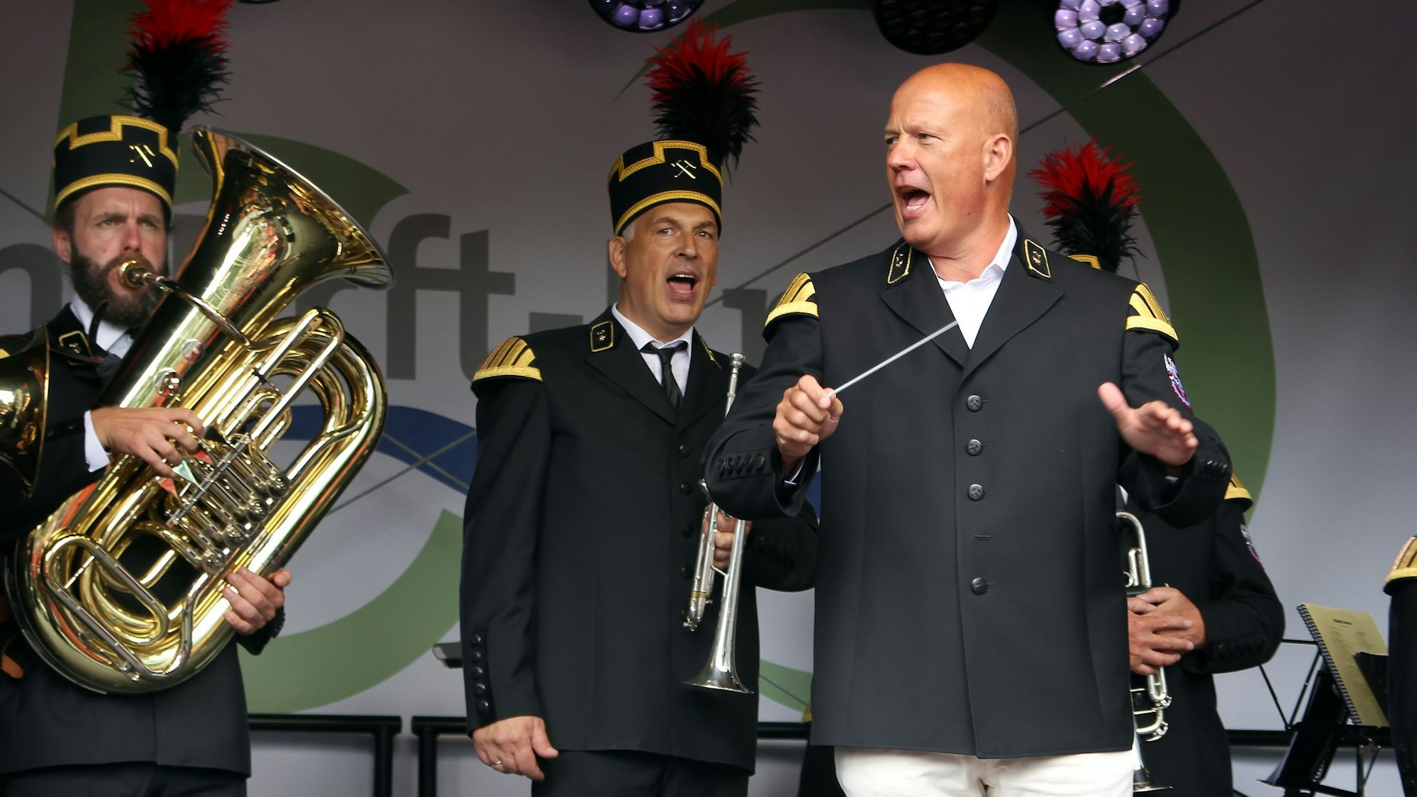 Das Foto zeigt Landrat Frank Rock, der in Uniformjacke auf der Bühne die Bergmannskapelle dirigiert.