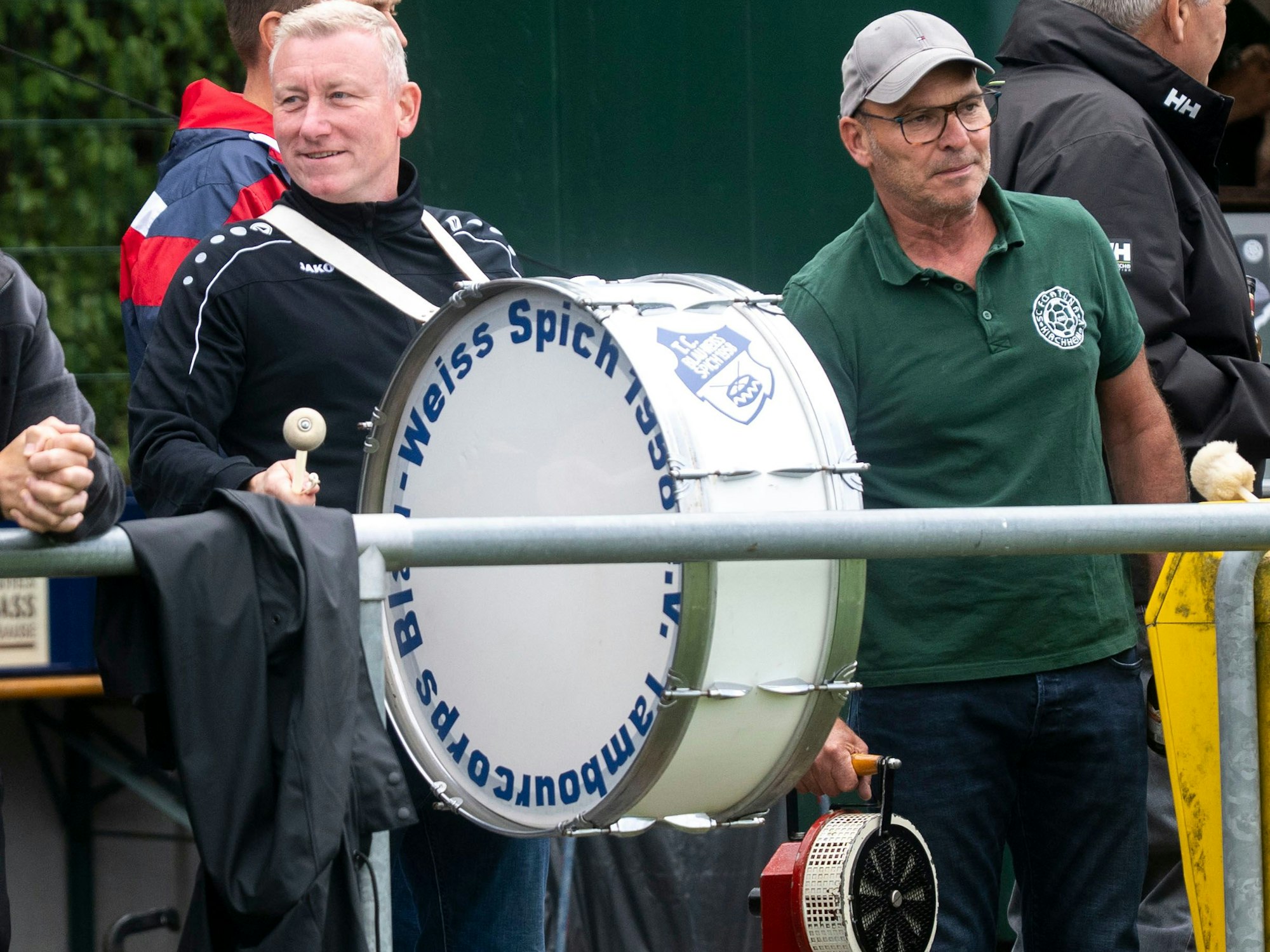 Ein Fußballfan hat eine dicke Trommel um den Hals hängen, der andere eine Sirene in der Hand.