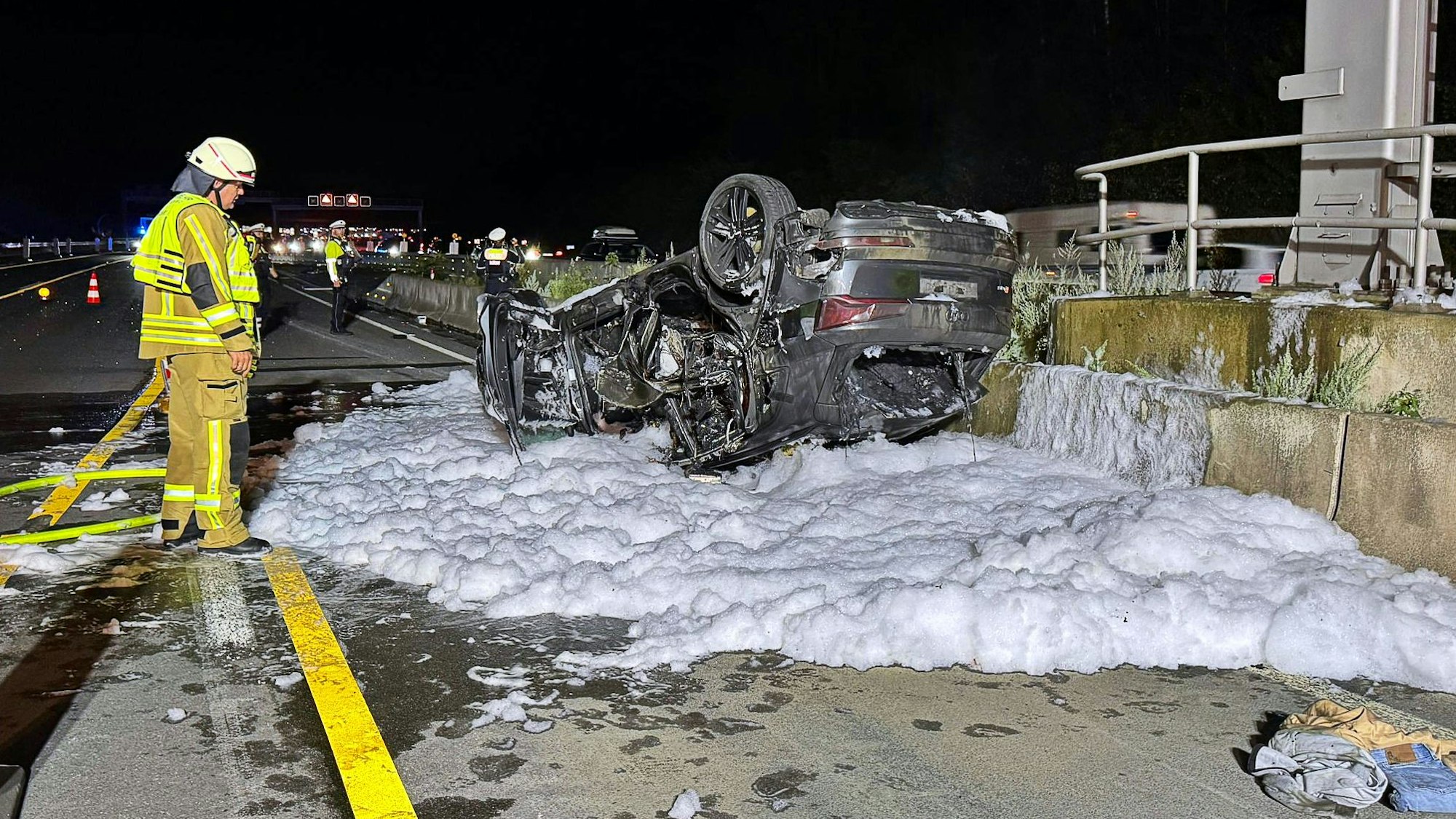 Ein ausgebranntes Auto liegt nach einem Unfall auf der Autobahn 3 im Löschschaum. (Archivbild)