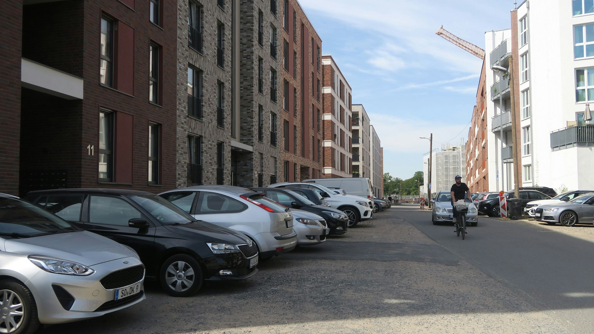Autos stehen links und rechts von einer Straße, an deren Seiten neue mehrstöckige Häuser stehen.
