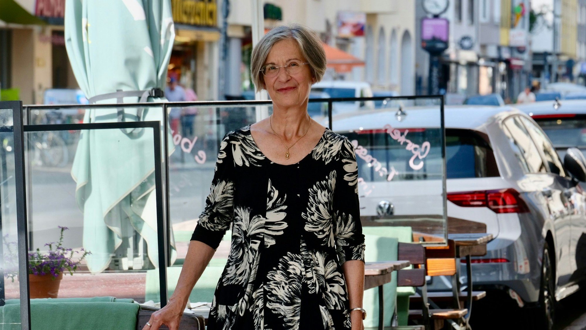 Ein Frau im Kleid steht an einer Straße, an der viele Autos parken.