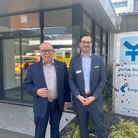 Zwei Männer stehen vor dem Eingang eines Krankenhauses.