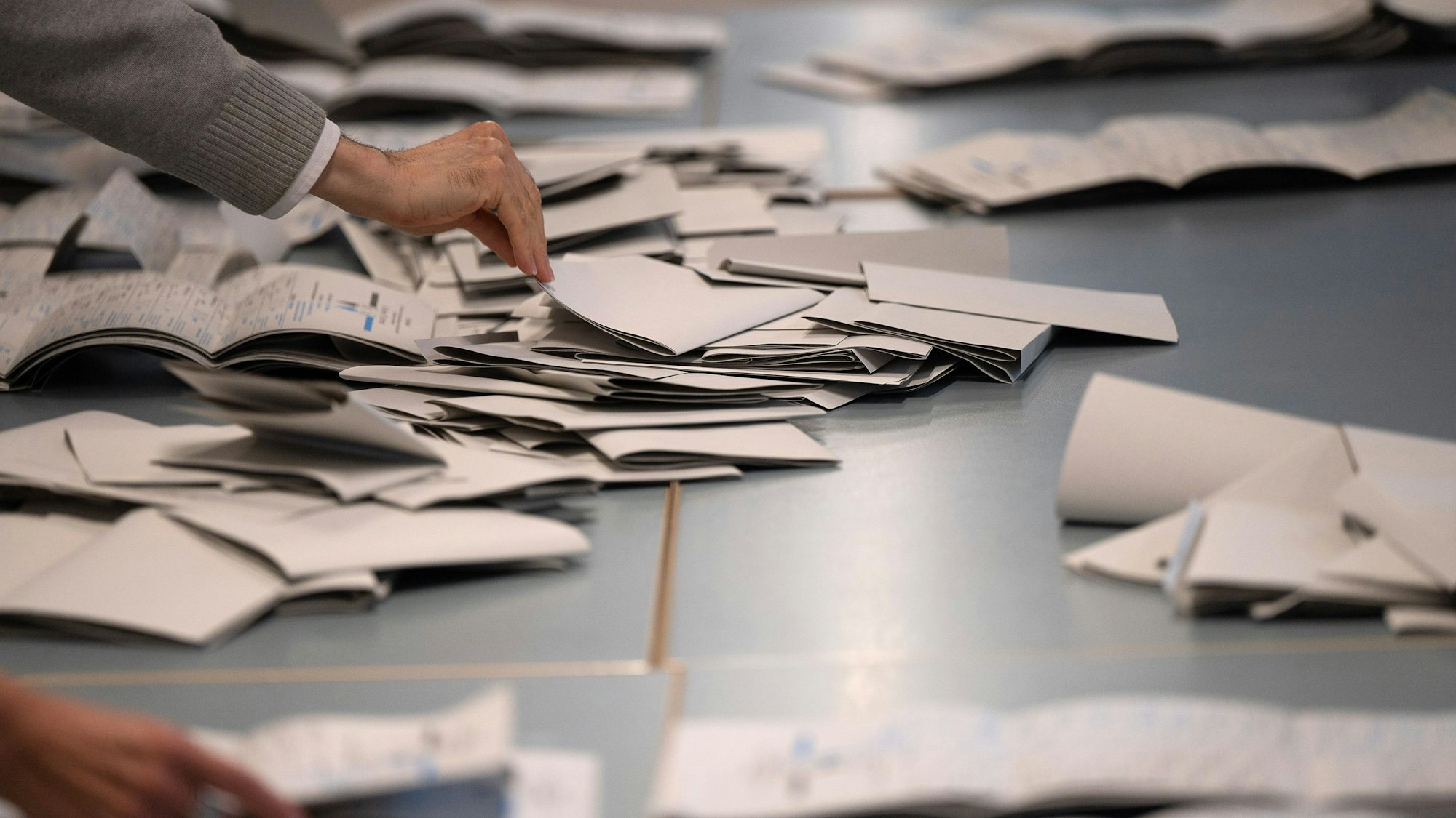 Symbolbild: Wahlhelfer und Wahlhelferinnen zählen in einem Wahllokal Stimmzettel.