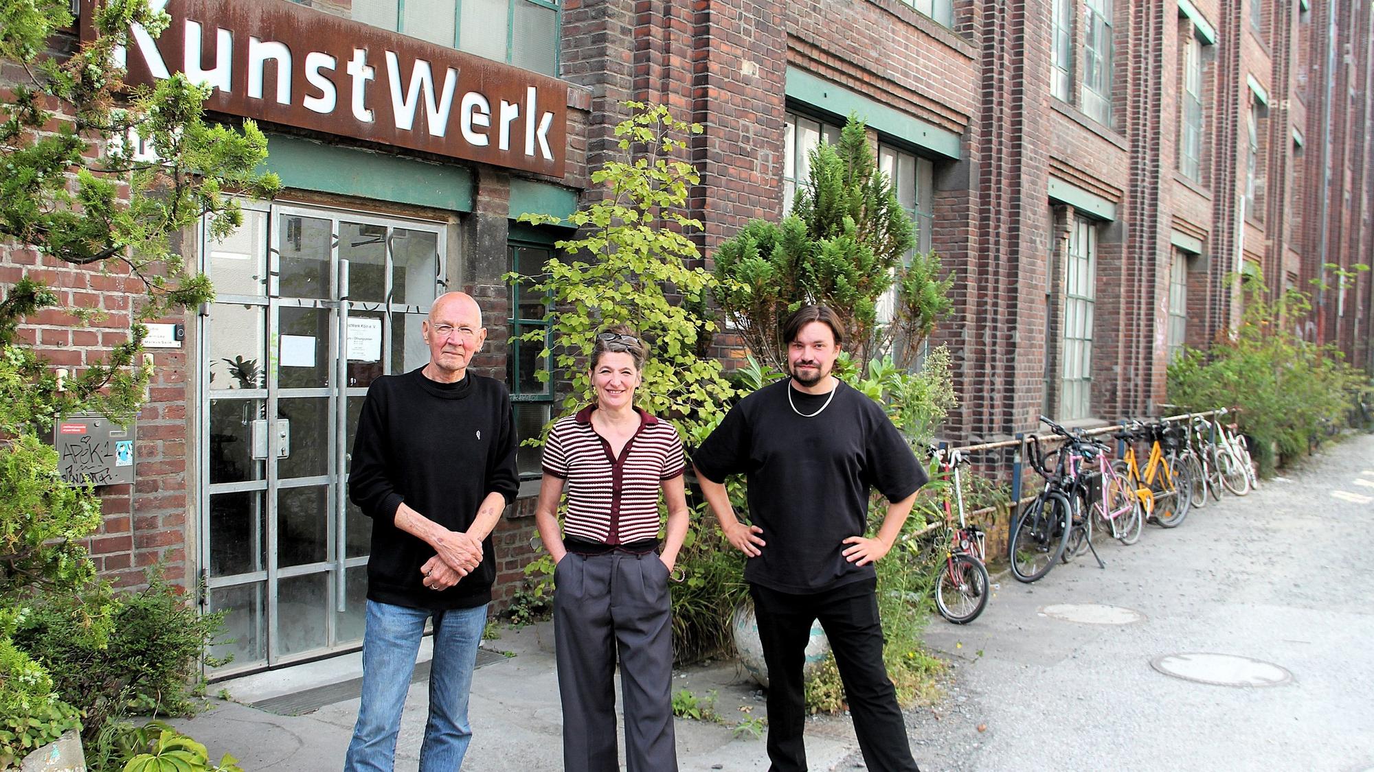 Eine Frau und zwei Männer stehen vor einem Backstein-Gebäudeeingang. Über der Eingangstür steht KunstWerk.