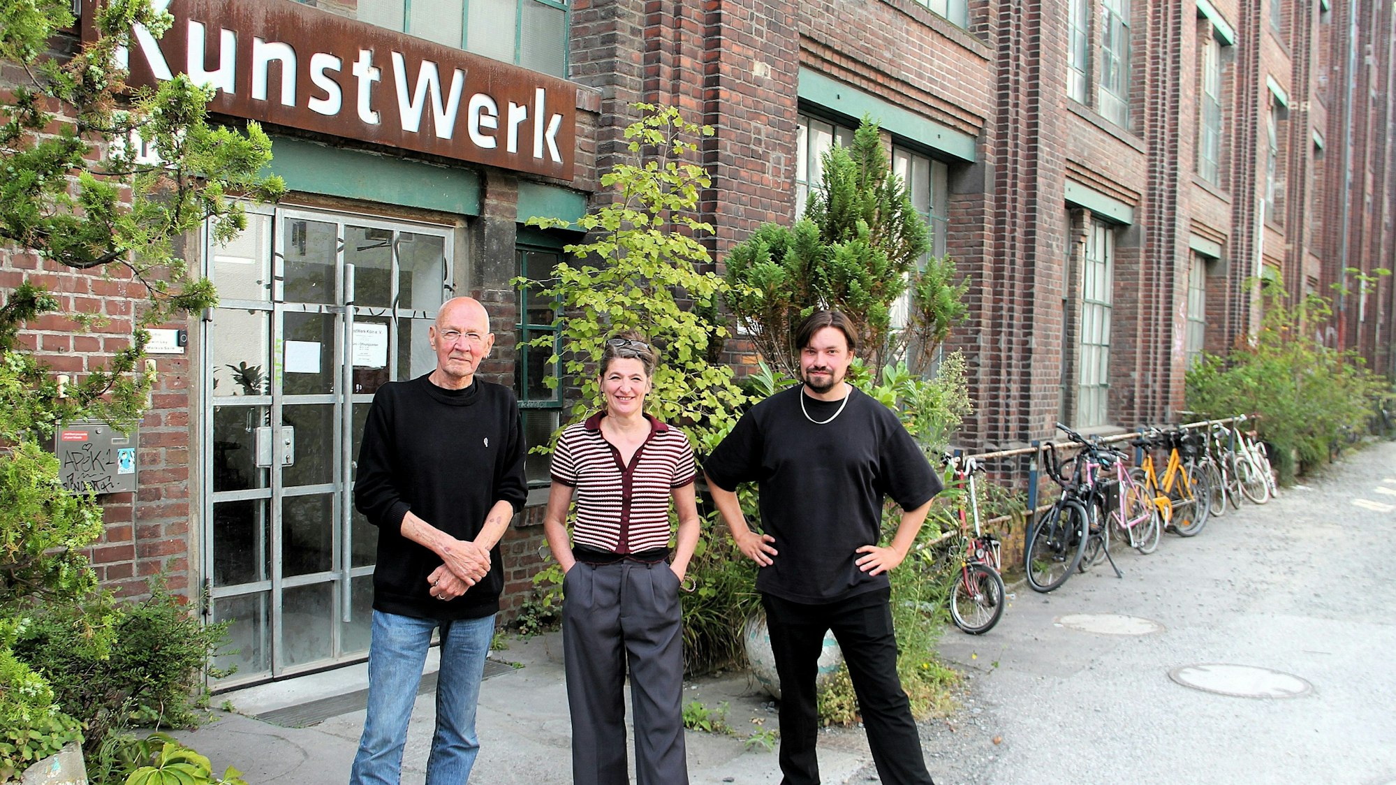 Eine Frau und zwei Männer stehen vor einem Backstein-Gebäudeeingang. Über der Eingangstür steht KunstWerk.