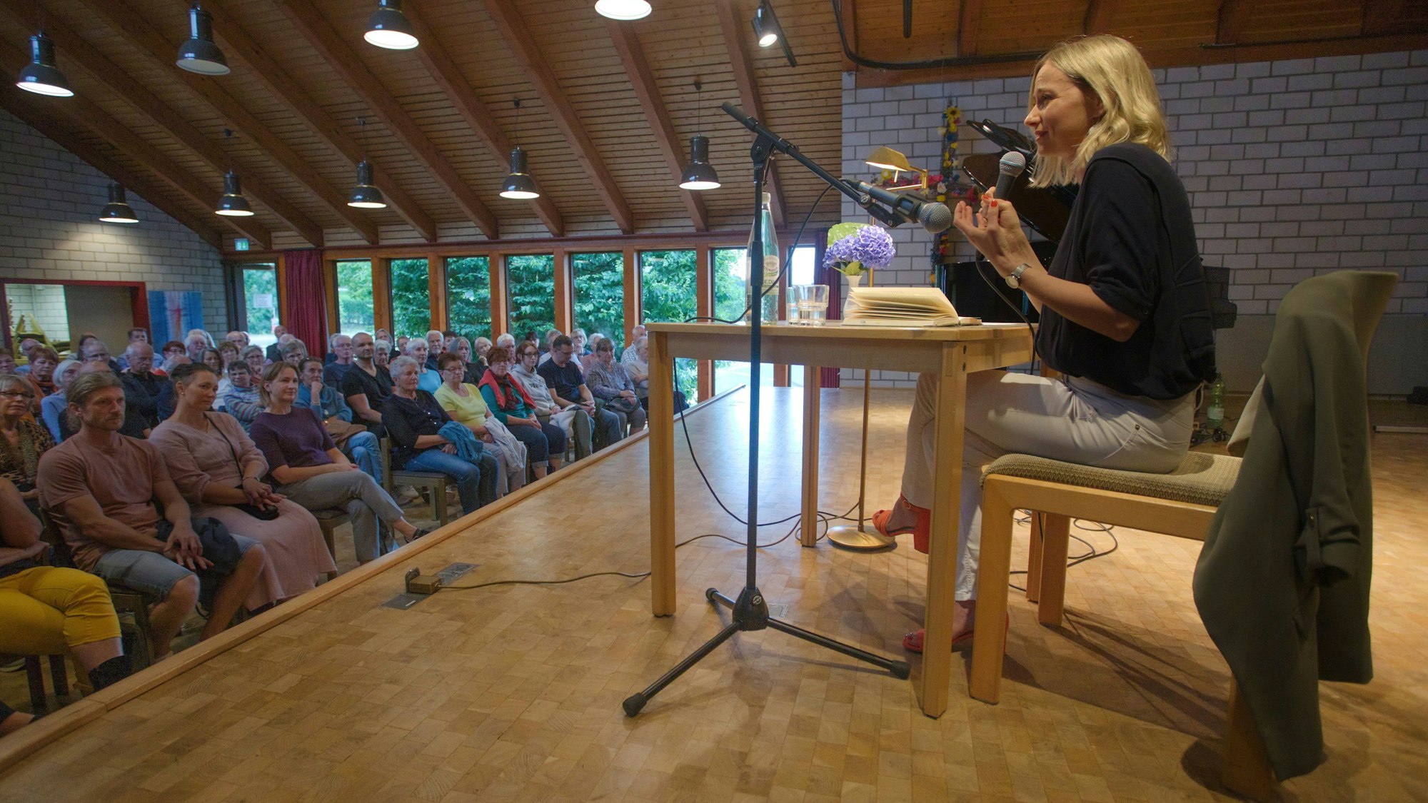 Die Journalistin Ira Peter sitzt auf der Bühne. Vor ihr sitzen viele Menschen, die ihr beim Vorlesen zuhören.