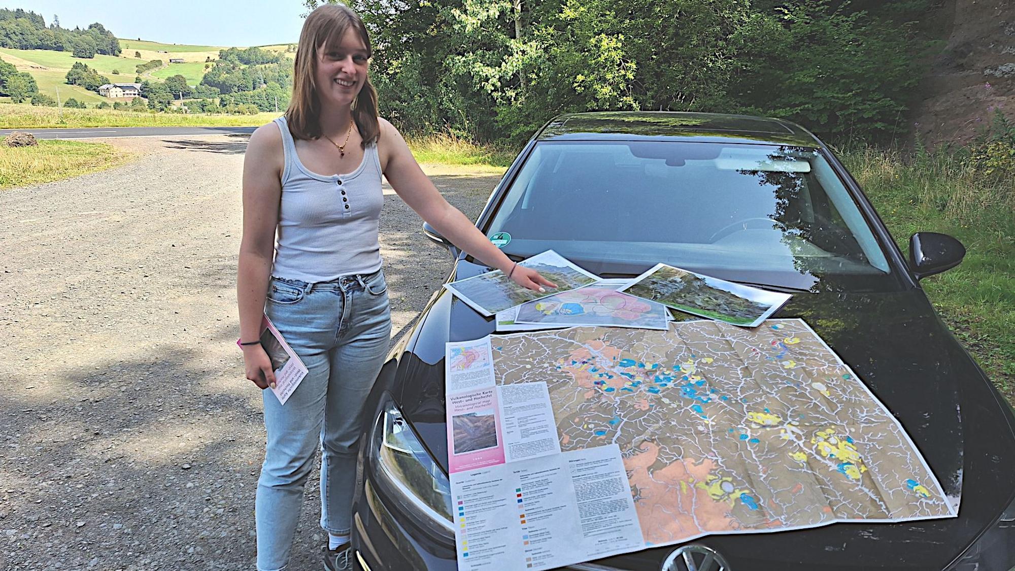 Eine Frau steht an einem Auto, auf dessen Motorhaube sie eine Landkarte ausgebreitet hat.