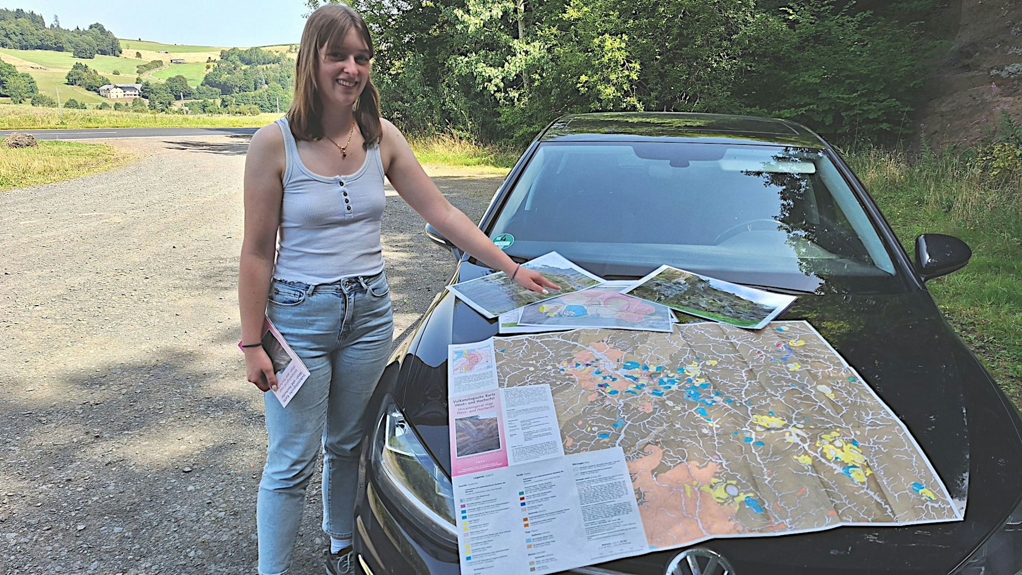 Eine Frau steht an einem Auto, auf dessen Motorhaube sie eine Landkarte ausgebreitet hat.