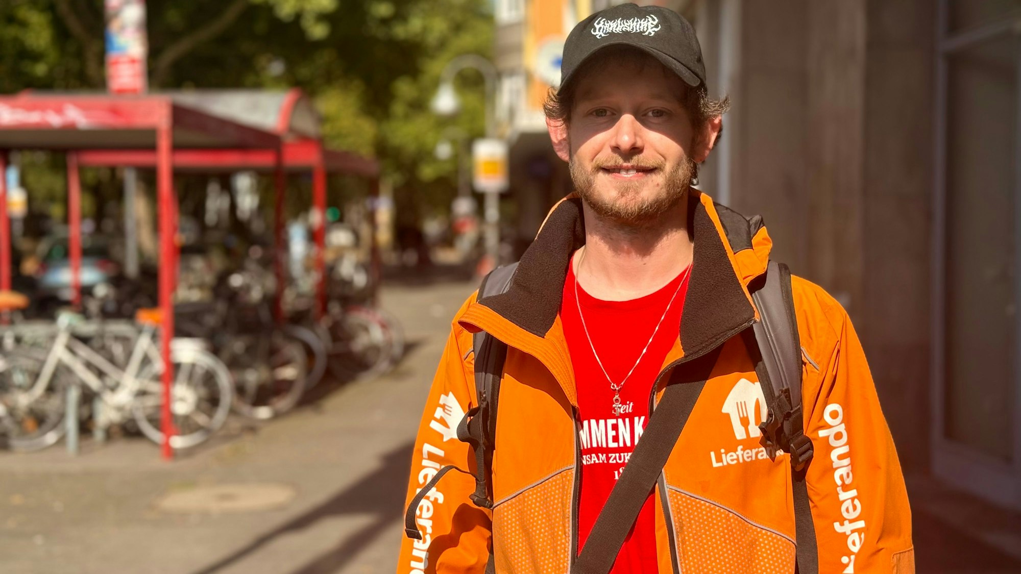 Fabian Schmitz trägt eine orange Weste von Lieferando und lächelt in die Kamera.