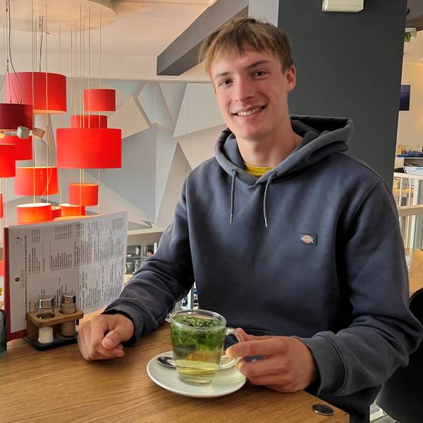 Das Bild zeigt einen jungen Mann mit einer Tasse Tee in einem Café.