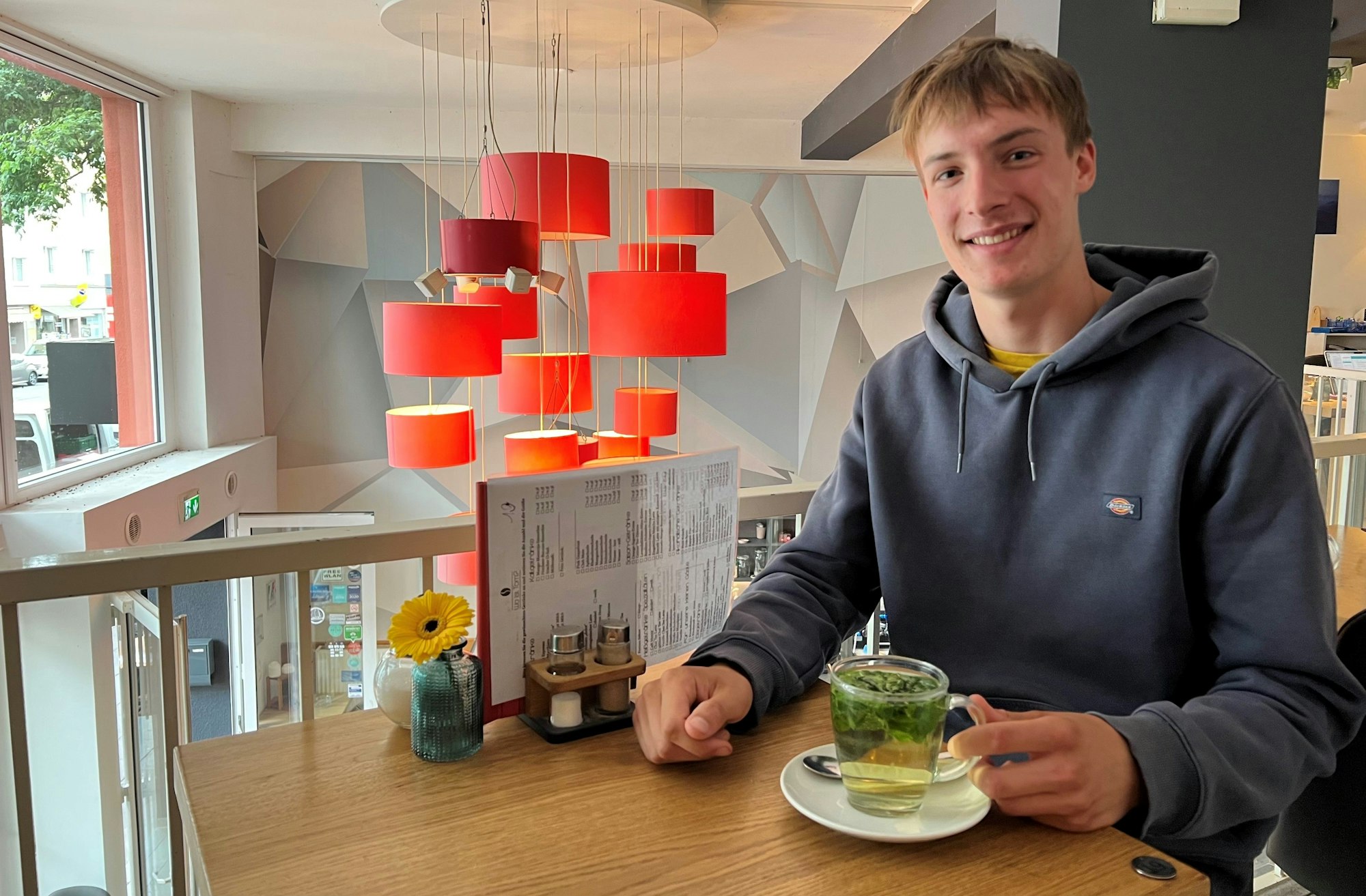 Das Bild zeigt einen jungen Mann mit einer Tasse Tee in einem Café.