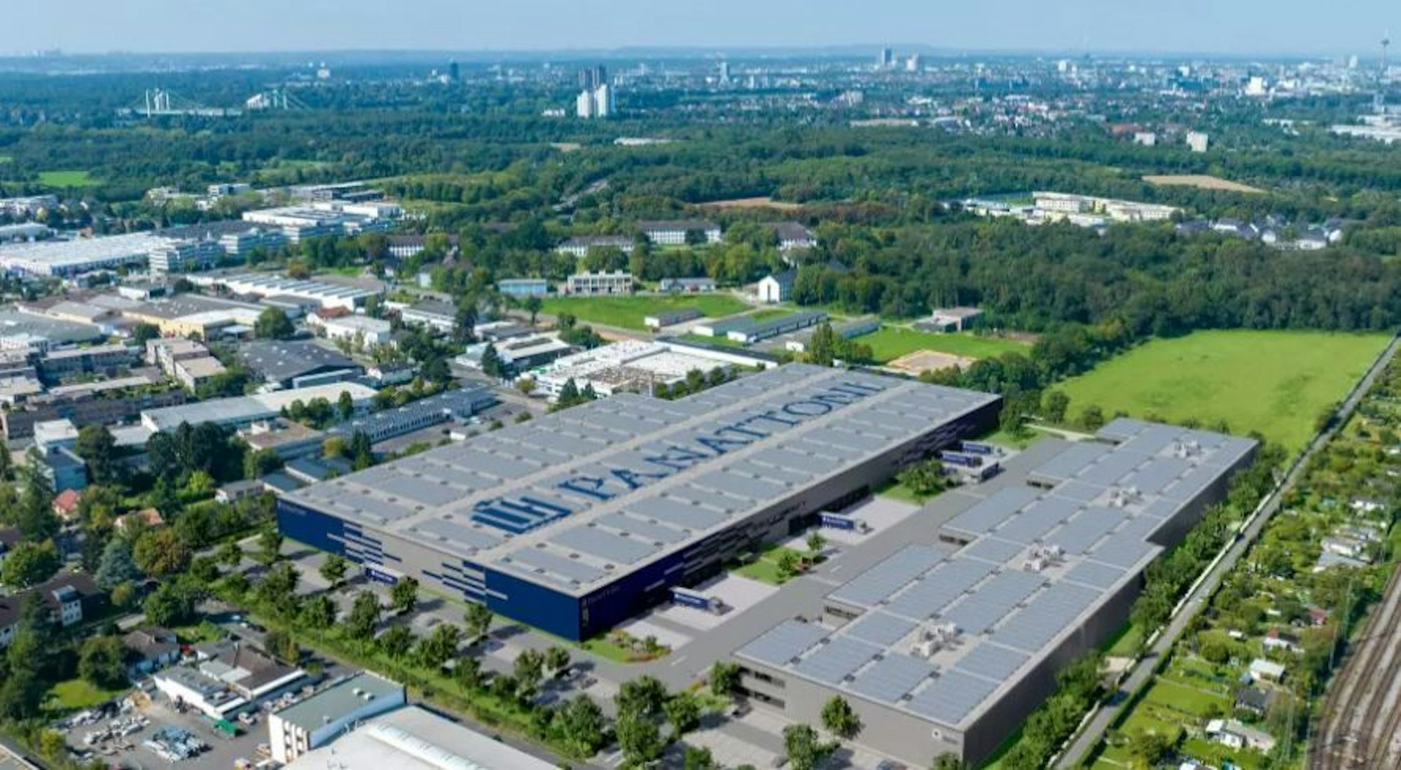 Ein Luftbild zeigt zwei große Industriehallen neben Wiesen und Bäumen.