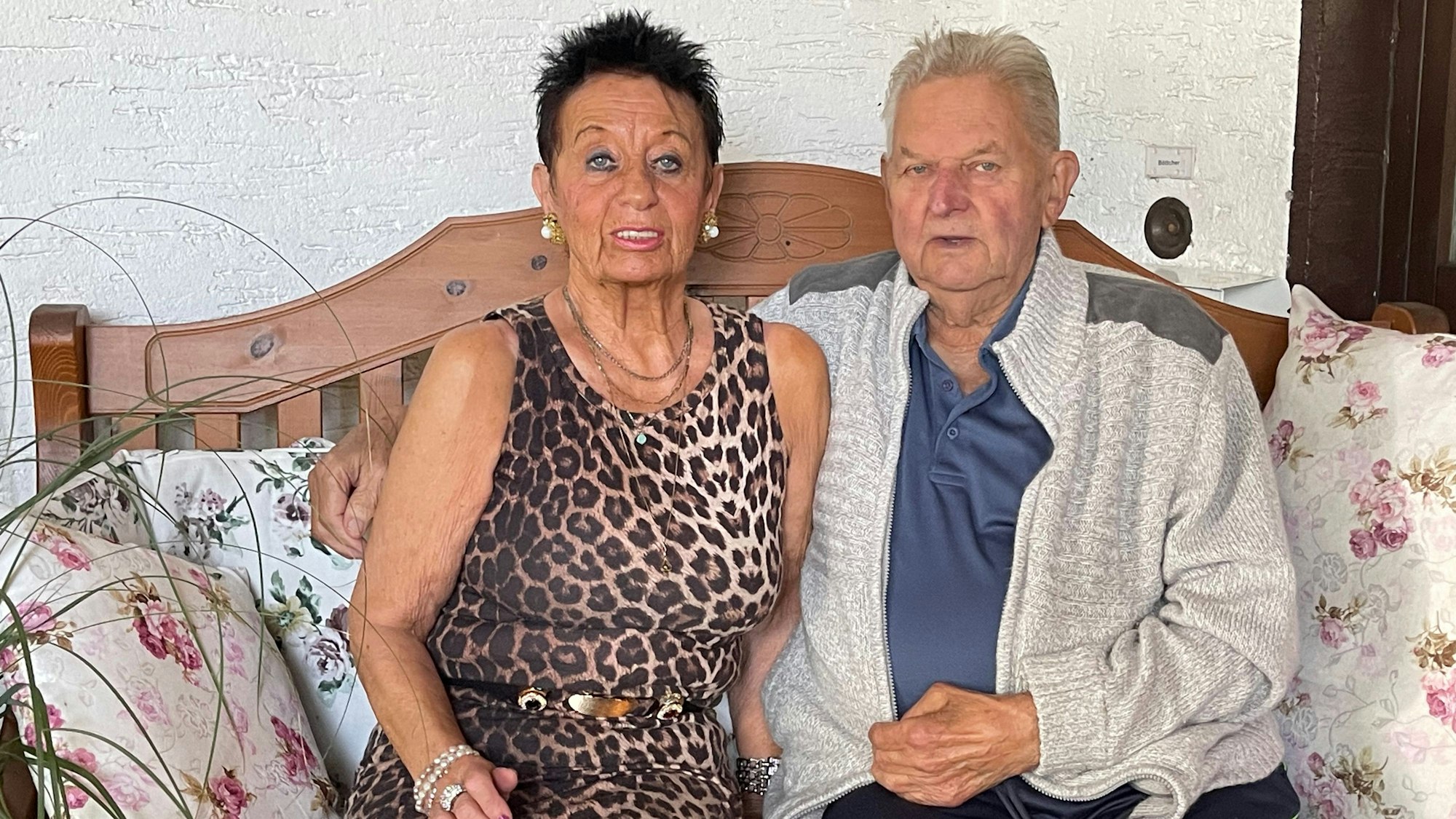 Das Ehepaar sitzt auf einer Bank vor ihrem Haus.