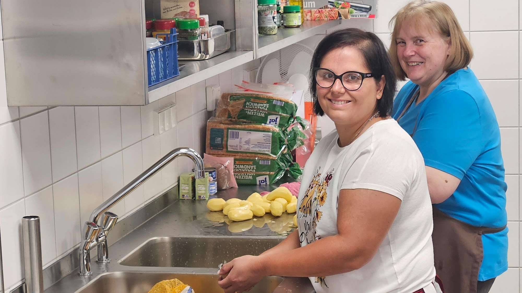 Andrea Schmidt (r.) und Antonella Risicato stehen an einer Arbeitsplatte nebeneinander und schälen Kartoffeln.