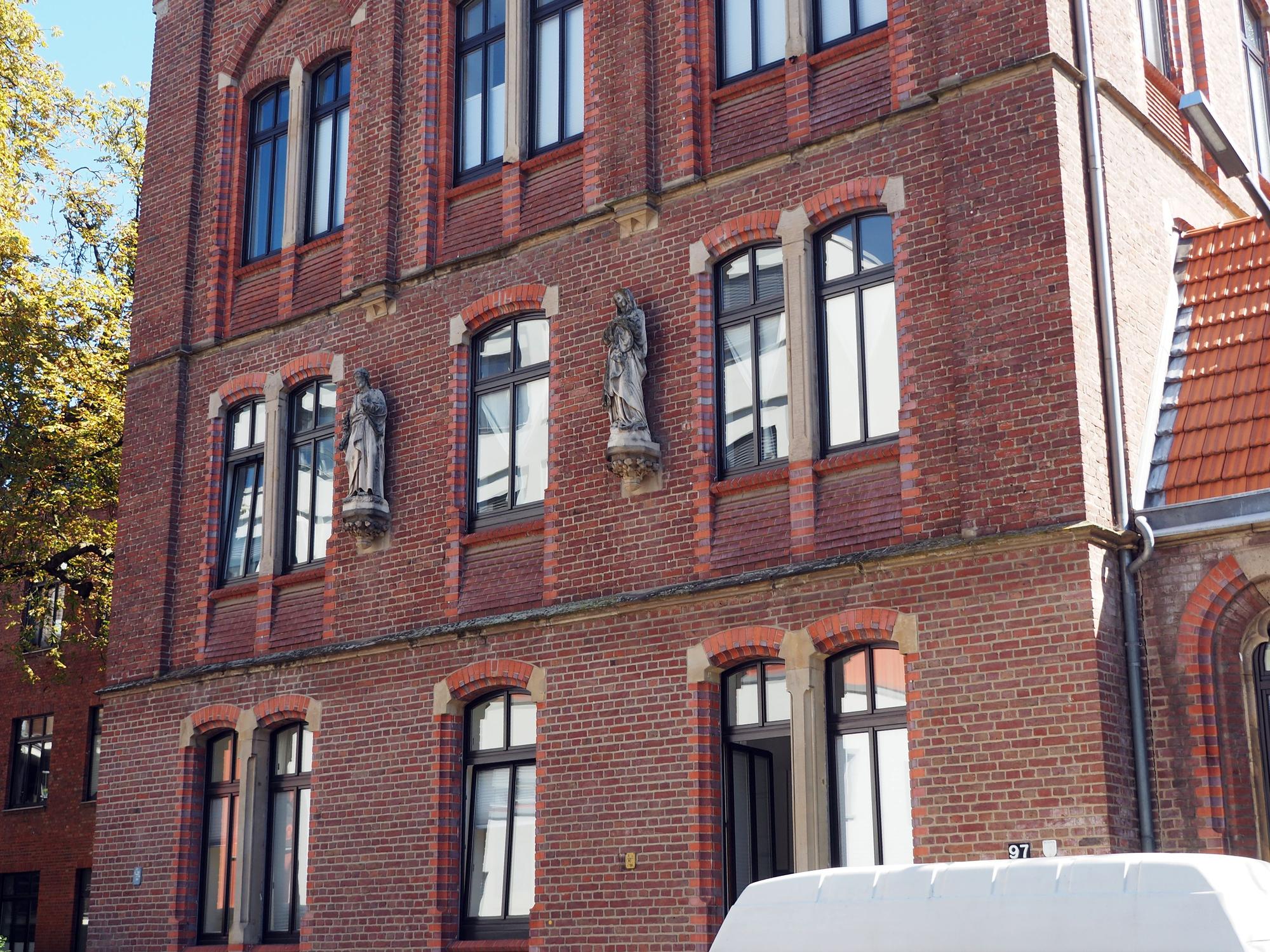 Ein Haus mit Backstein-Fassade hat mehrere Geschosse, an der Fassade sind zwei Statuen.