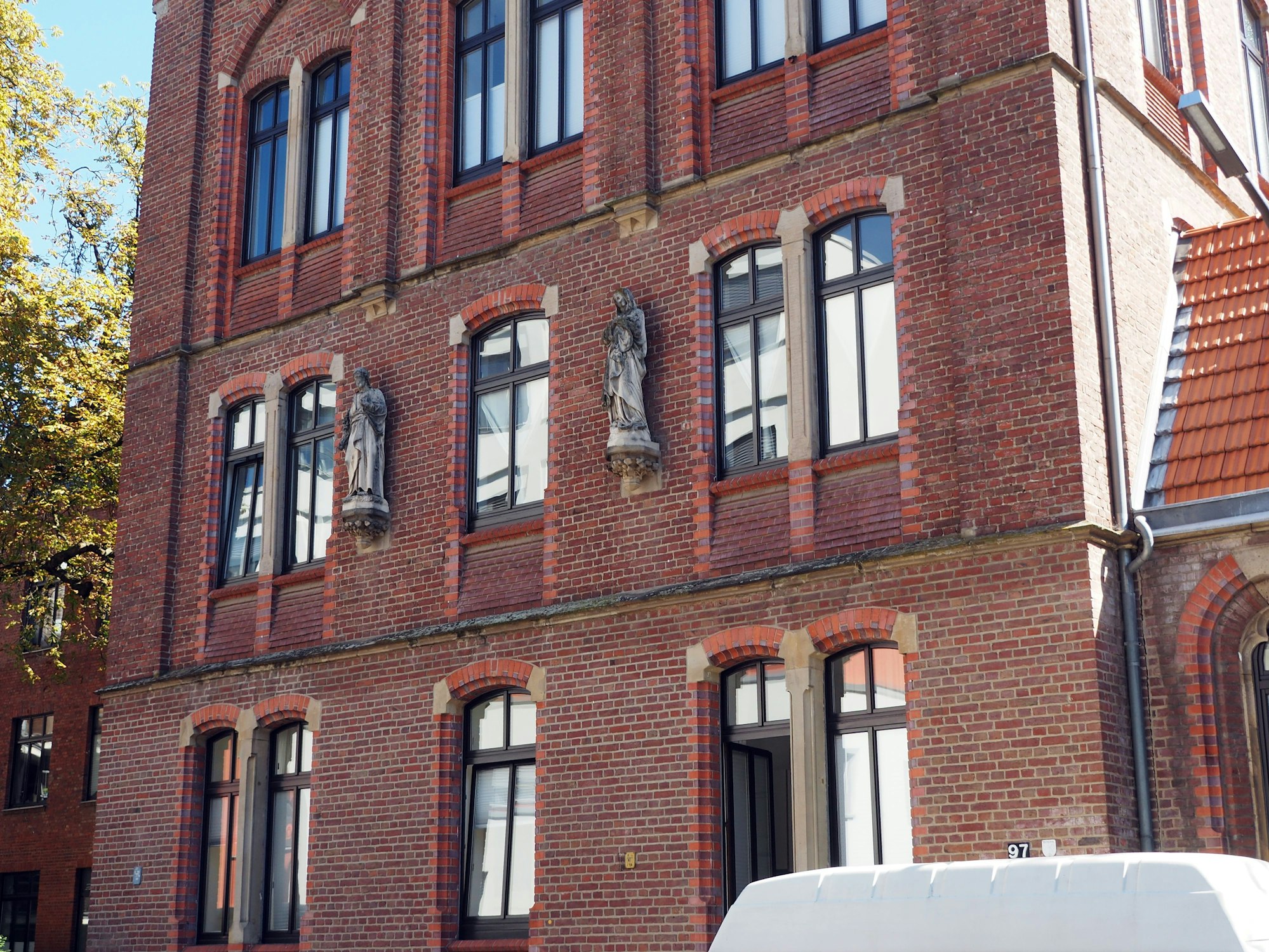 Ein Haus mit Backstein-Fassade hat mehrere Geschosse, an der Fassade sind zwei Statuen.