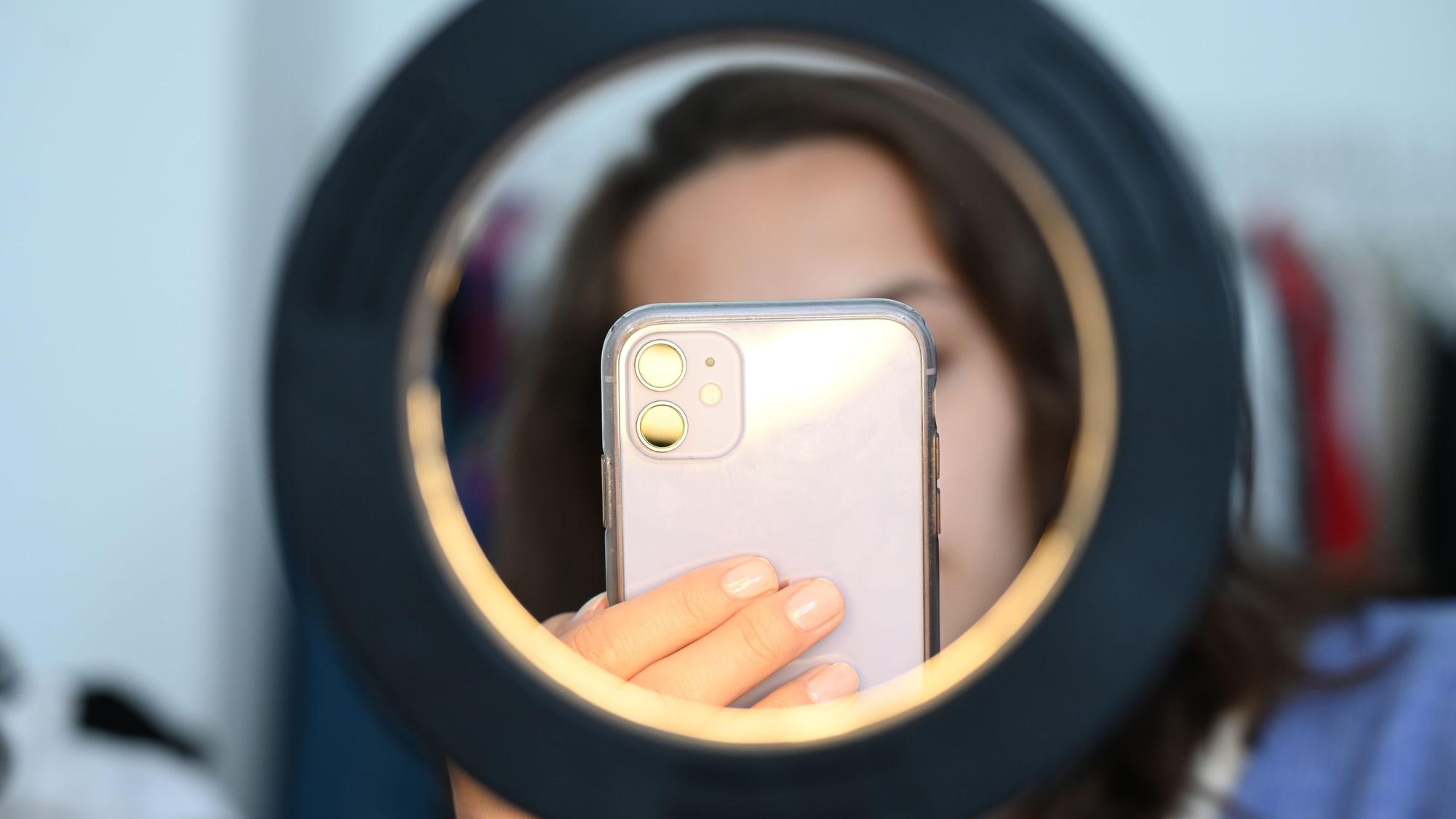 Eine Influencerin sitzt hinter einem Ringlicht und macht dabei Aufnahmen von sich.