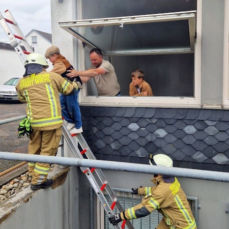 Ein Mann hilft einem Kind beim Abstieg über eine Feuerwehrleiter.