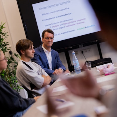 Hendrik Wüst (CDU), Ministerpräsident von Nordrhein-Wetsfalen, besucht im Schülerinnen und Schüler der 12. Klasse der Geamtschule Bochum Mitte, die ihr Abitur machen wollen. Neben ihm sitzt der Schüler Taylor.