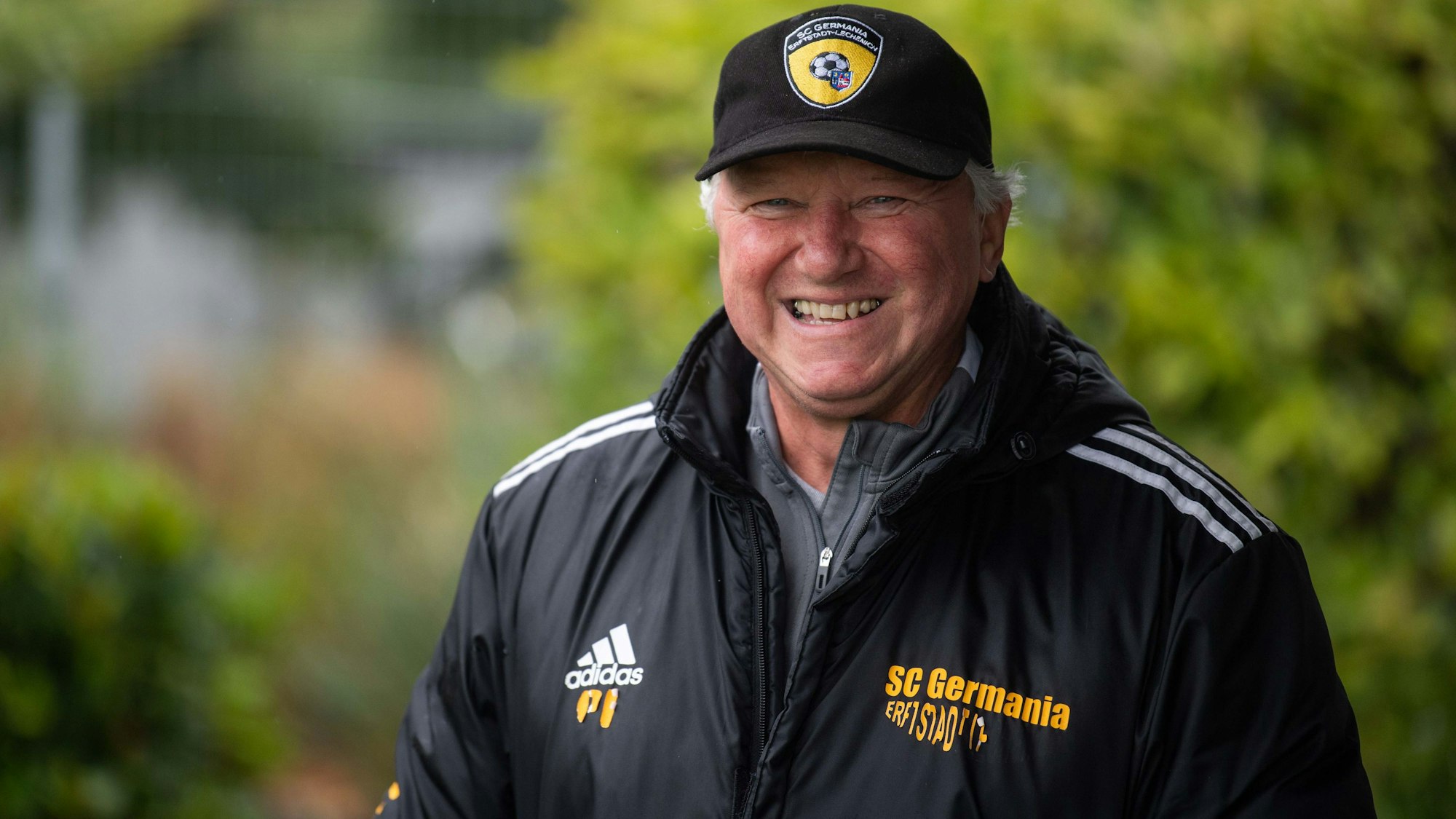 Paul Esser trägt Kappe und Jacke mit Erftstadt-Lechenich-Logo und -Schriftzug und lacht.