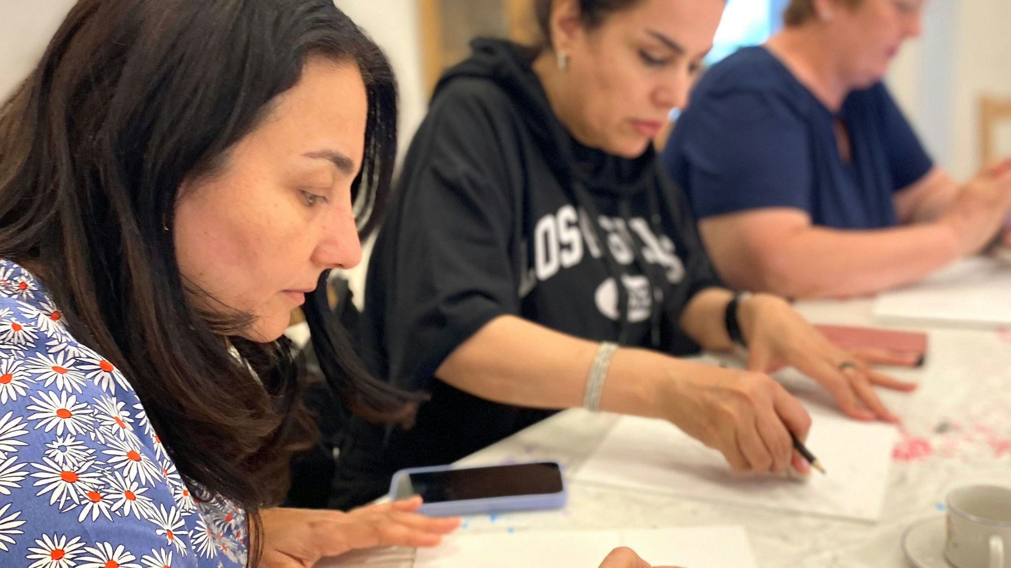 Drei Frauen sitzen zeichnend an einem Tisch und schauen sehr konzentriert.