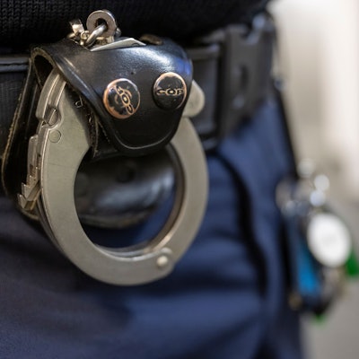 Eine Handschelle hängt am Gürtel eines Polizisten.