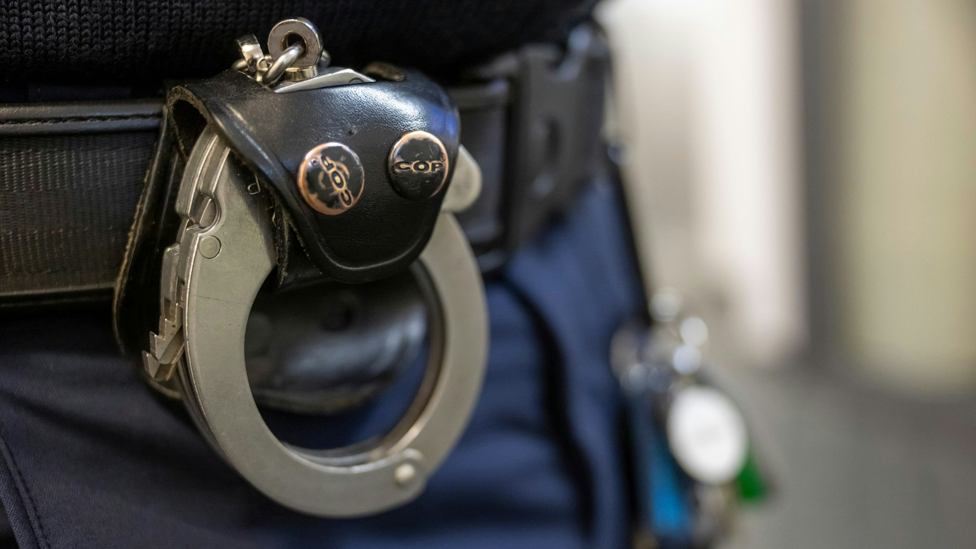 Eine Handschelle hängt am Gürtel eines Polizisten.