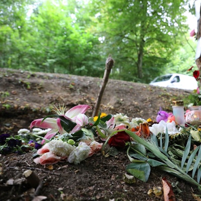 Blumen und Kerzen stehen an einem Baum in einer Kurve der Dürschtalstraße, in der am 16. August 2025 vier Teenager bei einem Unfall ums Leben kamen.