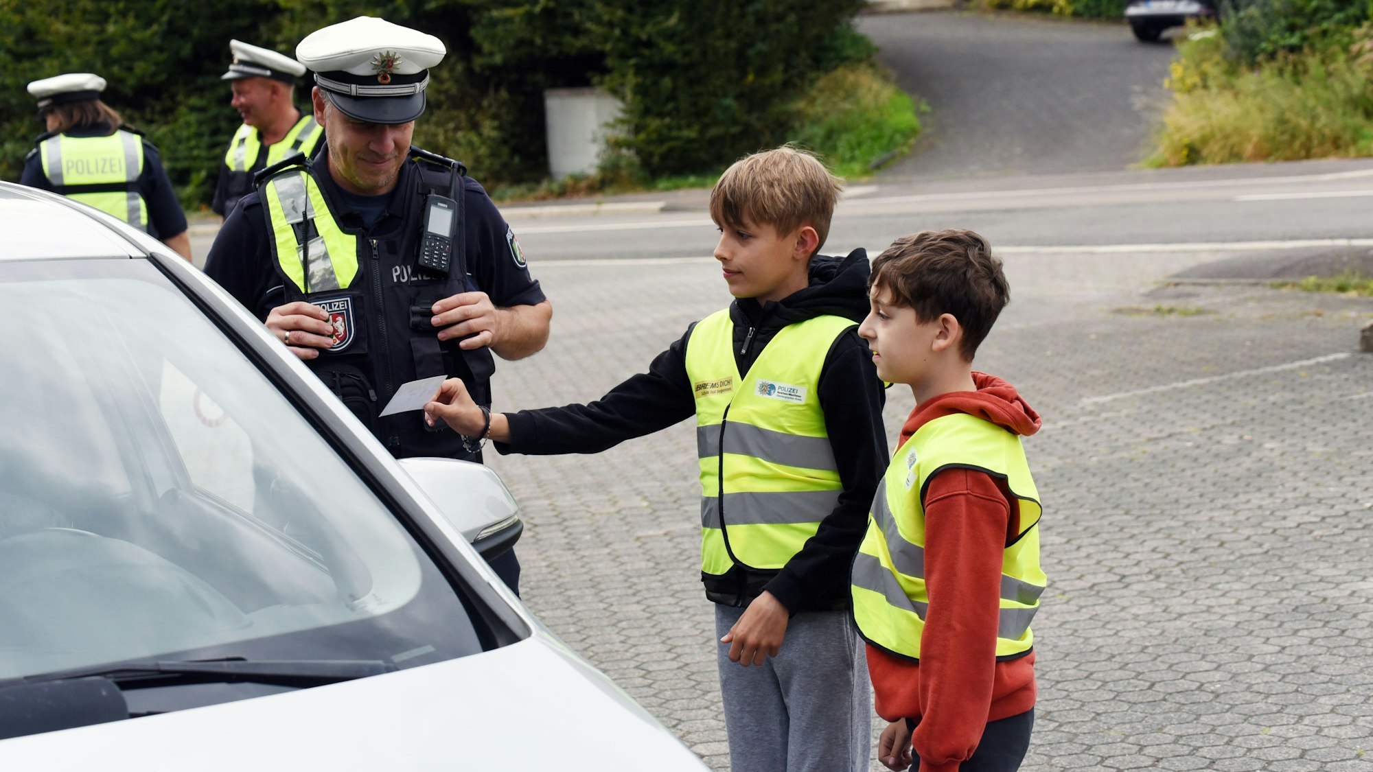 Das Foto zeigt zwei Schüler und Polizisten im Gespräch mit einem Autofahrer
