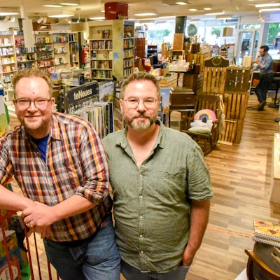 Das Foto zeigt die beiden Inhaber der Buchhandlung vor Bücherregalen in ihrem Geschäft.