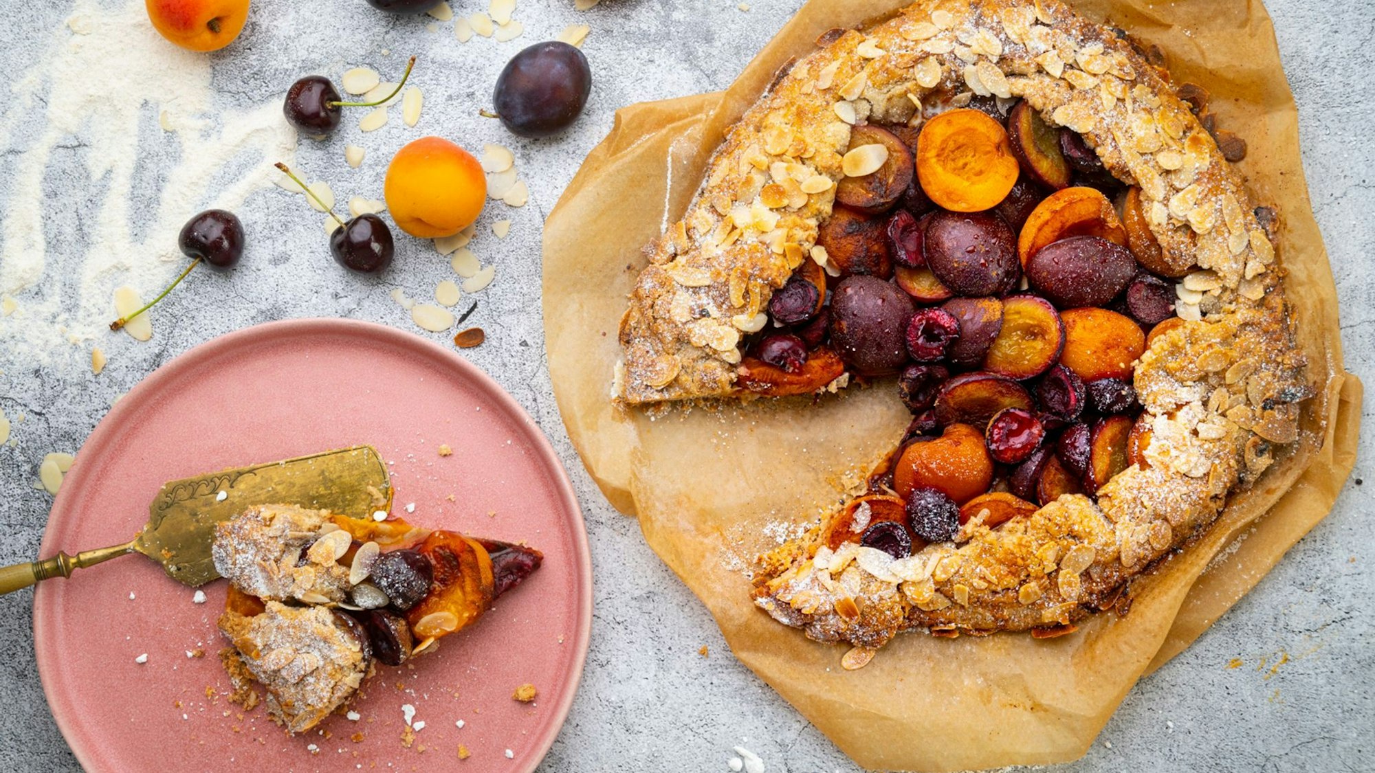 Galette mit süßem Steinobst aus Pflaumen und Aprikosen und späten Kirschen auf Backfolie und Teller.