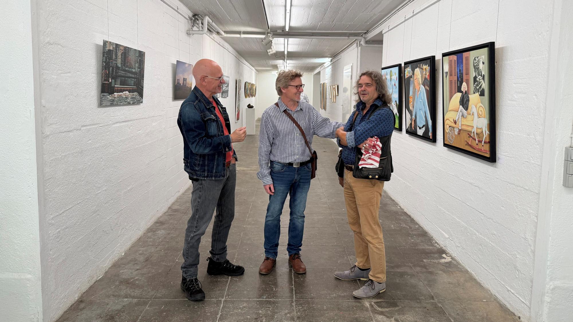 Drei der neuen Künstler des Vereins im Gang des Künstlerbunkers. Michael Brock (v.l.), Thomas Ernst und Norbert Küpper. An den Wänden hängen die Werke der Ausstellung.