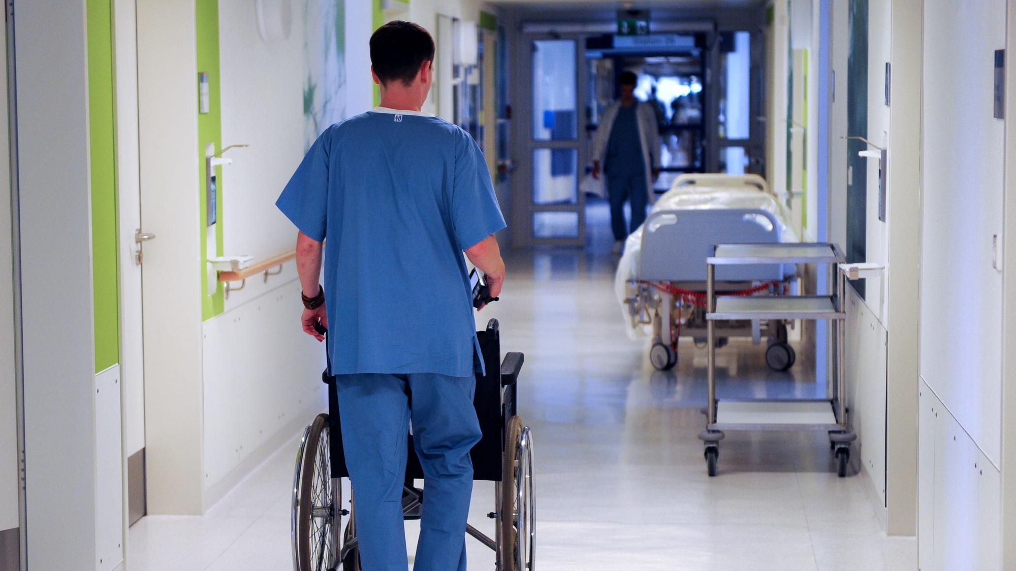 Ein Pfleger schiebt einen Rollstuhl über einen Flur in einem Krankenhaus.