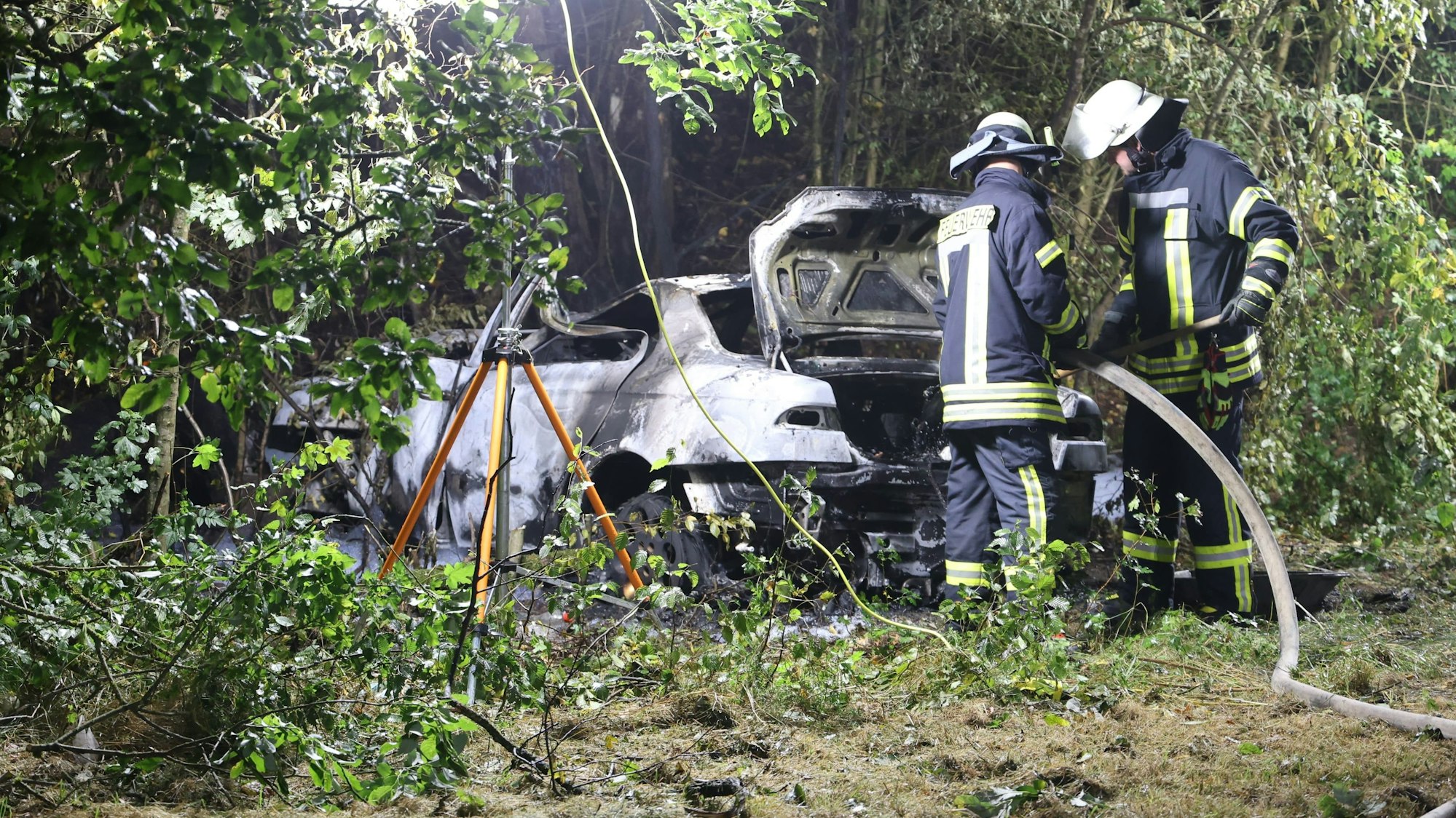 Das Bild zeigt zwei Feuerwehrmänner, die das Wrack löschen.