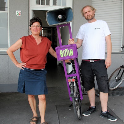 Eine Frau und ein Mann stehen nebeneinander, zwischen ihnen ein Fahrrad mit einem ungewöhnlichen Gepäckträger.