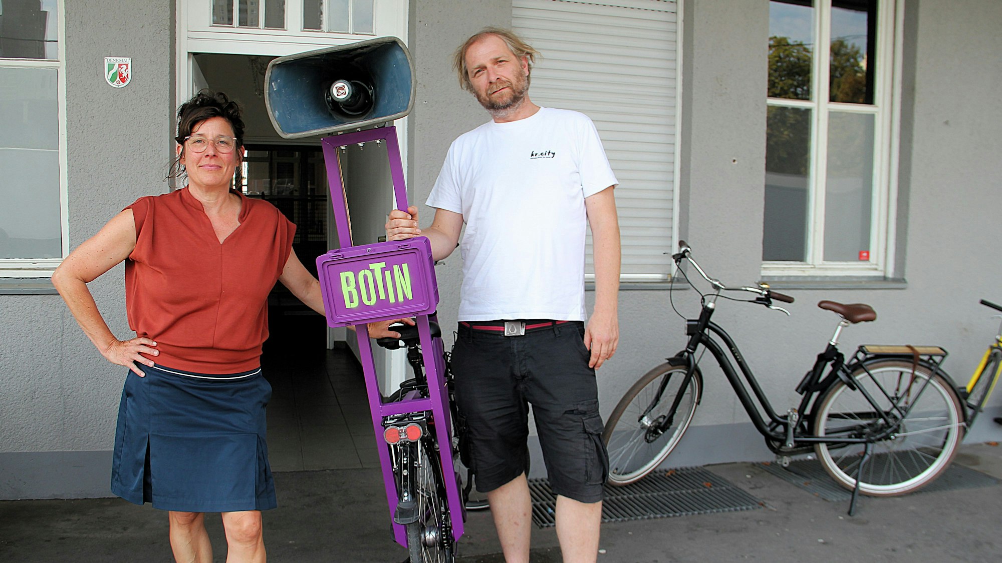 Eine Frau und ein Mann stehen nebeneinander, zwischen ihnen ein Fahrrad mit einem ungewöhnlichen Gepäckträger.