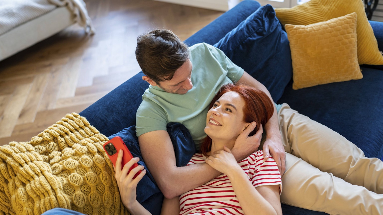 Junges Paar, das auf dem Sofa ruht und von der Zukunft träumt und das Eheleben genießt. Glücklich lächelnd liegt eine Frau auf dem Bauch eines Mannes.