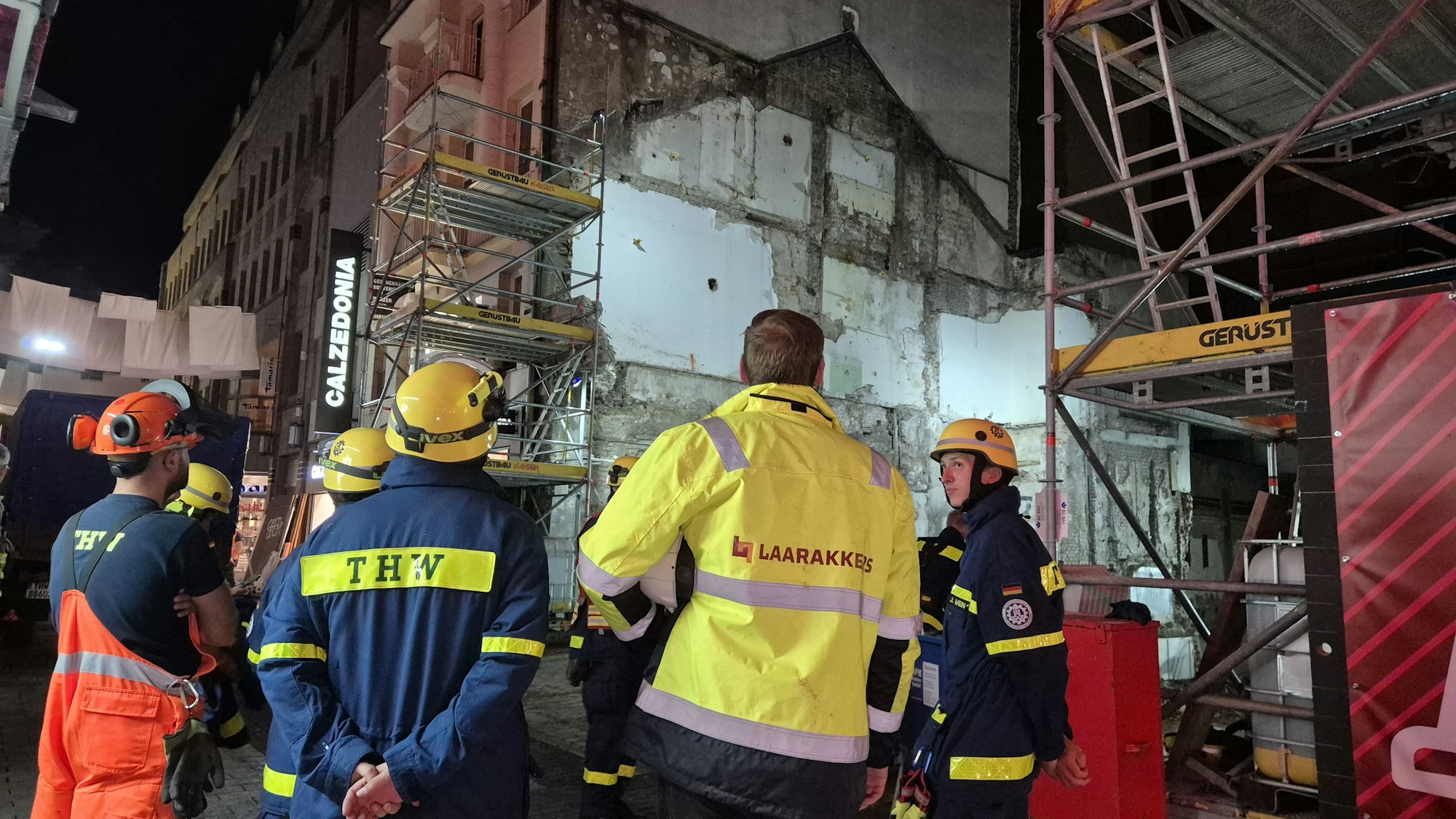 Einsatzkräfte des Technischen Hilfswerks und einer Baufirma stehen vor einer Hauswand, die möglicherweise einsturzgefährdet ist.